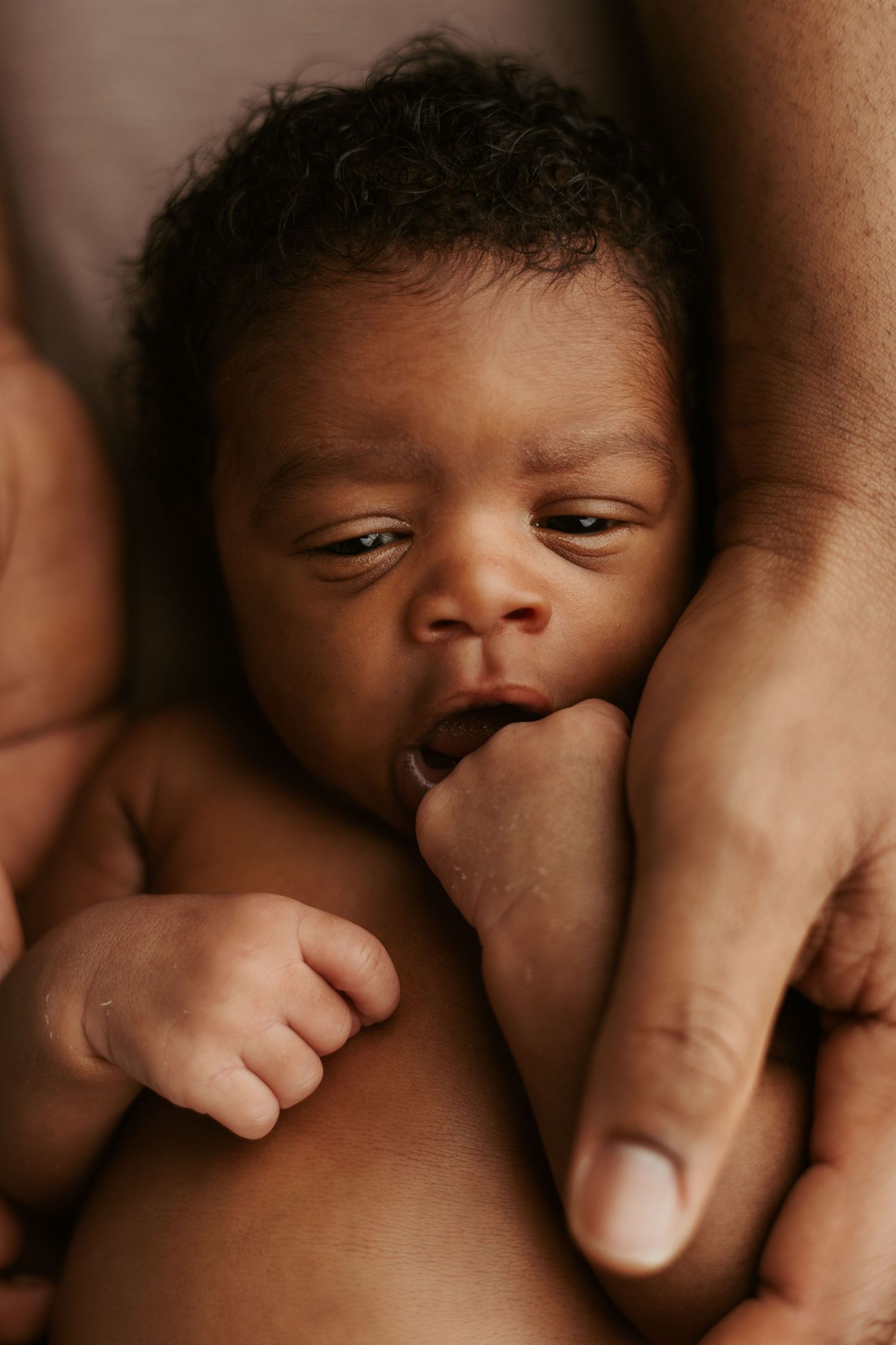 Close up portrait of newborn baby's face with gentle hands providing support.