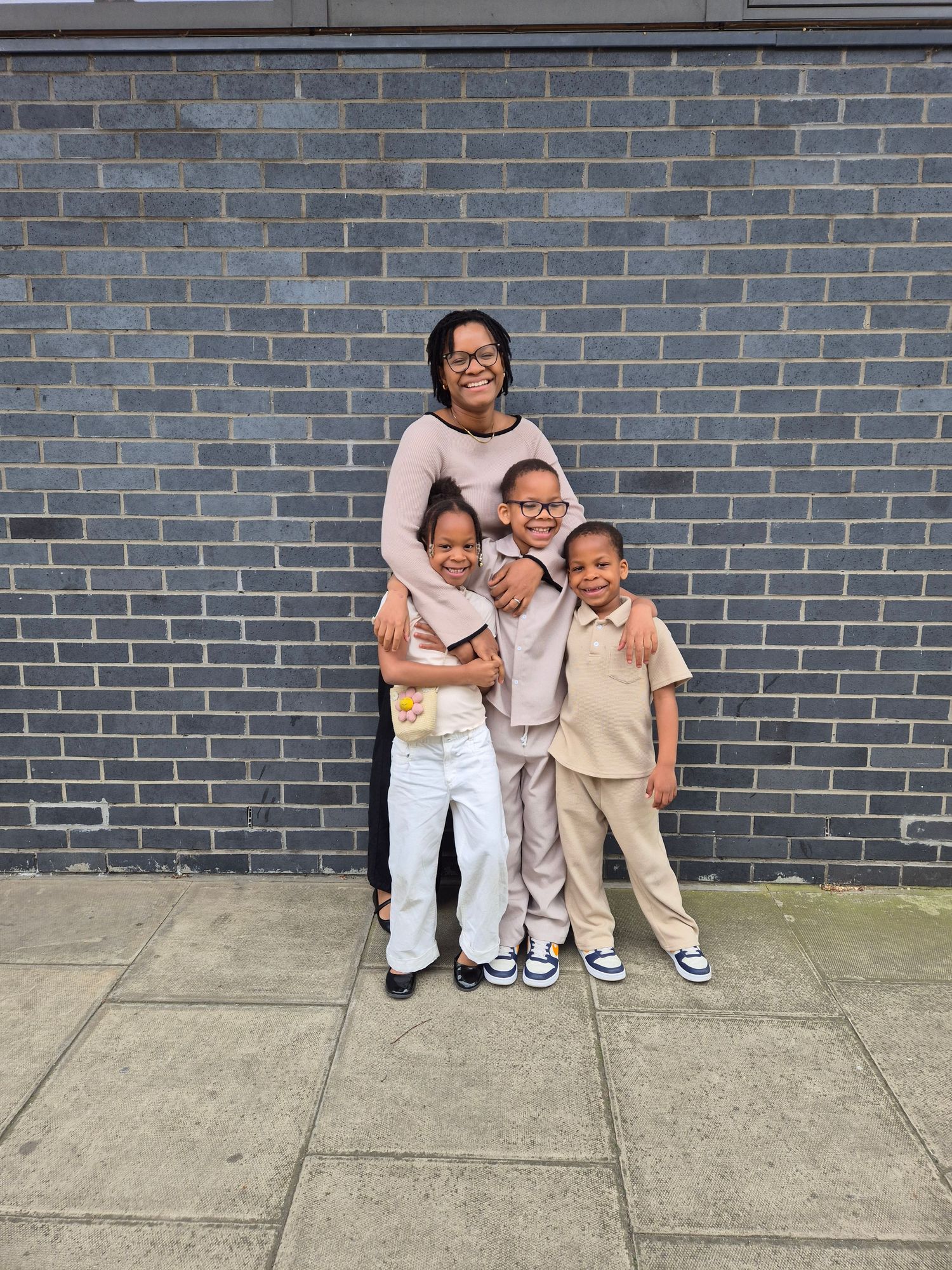 A family poses together against a gray brick wall on a concrete sidewalk.