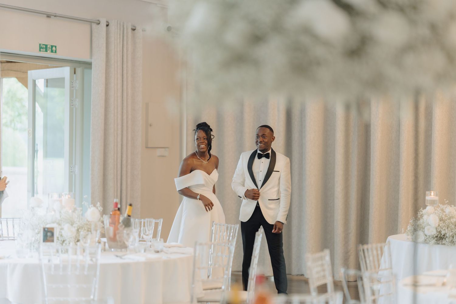 Wedding reception hall setup with white linens and floral arrangements on round tables.