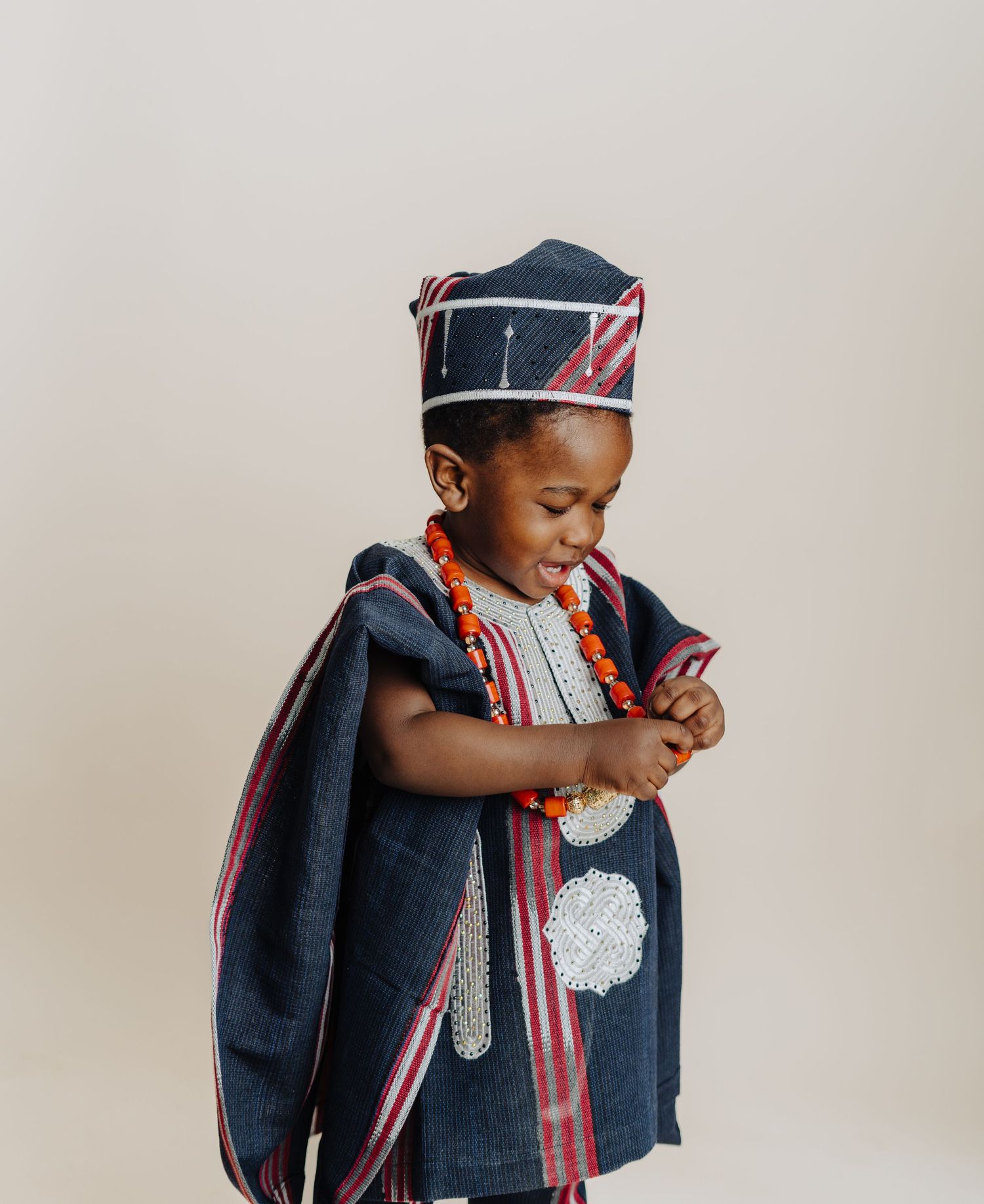 Child in traditional African dress looks down while playing with beaded necklace.
