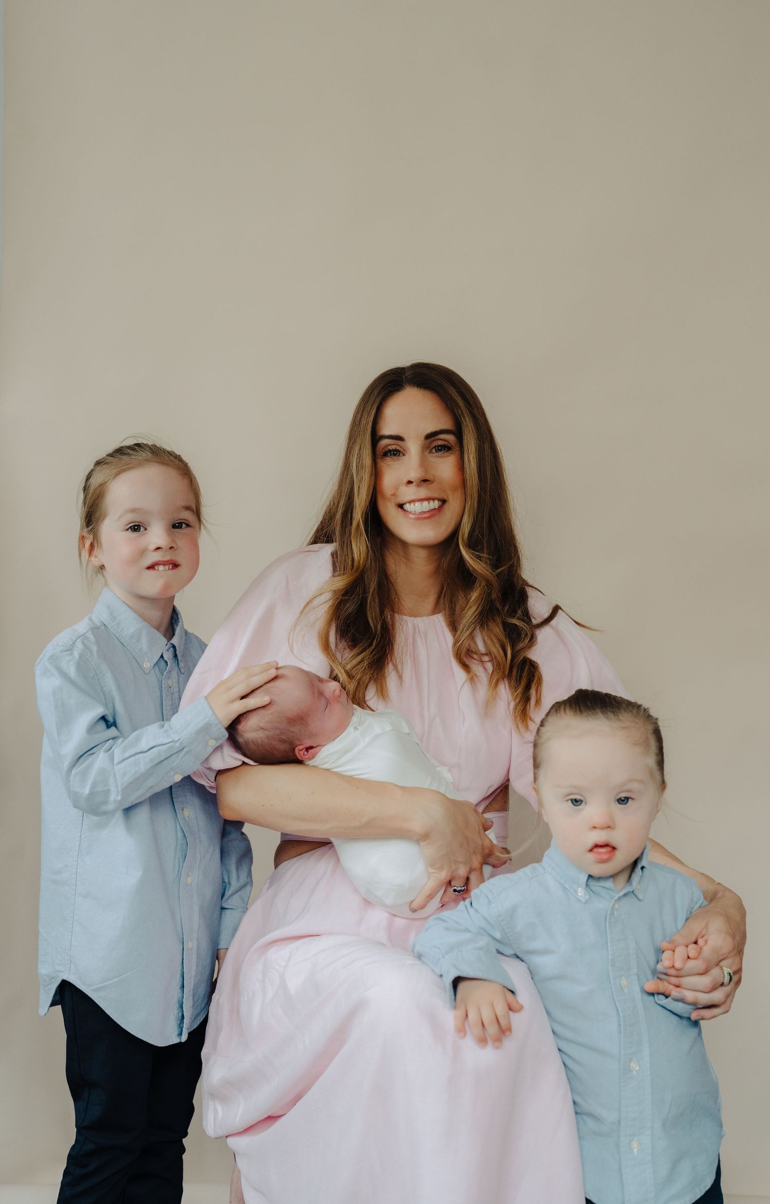 Family portrait series in soft lighting with children in blue and mother in pink dress.