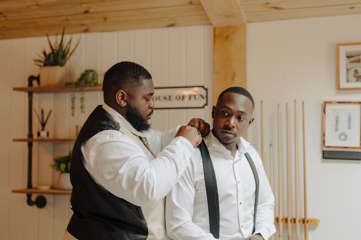 Groomsmen in white shirts and suspenders preparing in a rustic wooden interior.