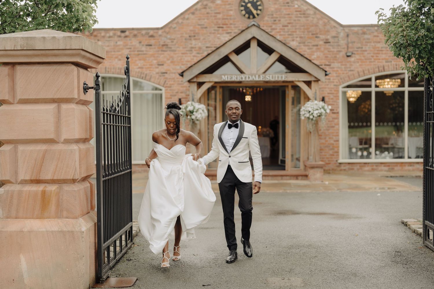 Wedding couple walking together outside a rustic brick venue entrance.