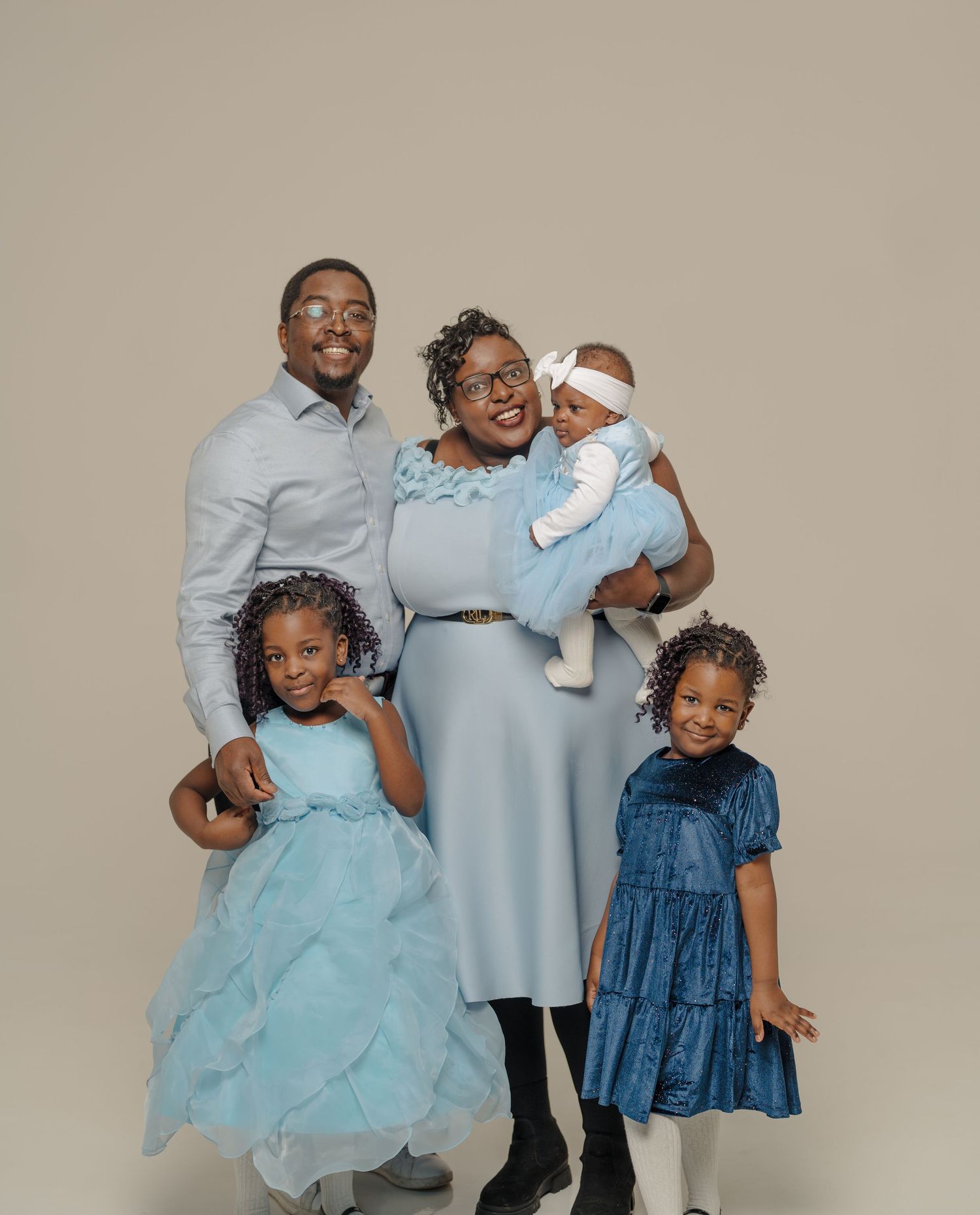 Family portrait with children in coordinating blue outfits against neutral background.