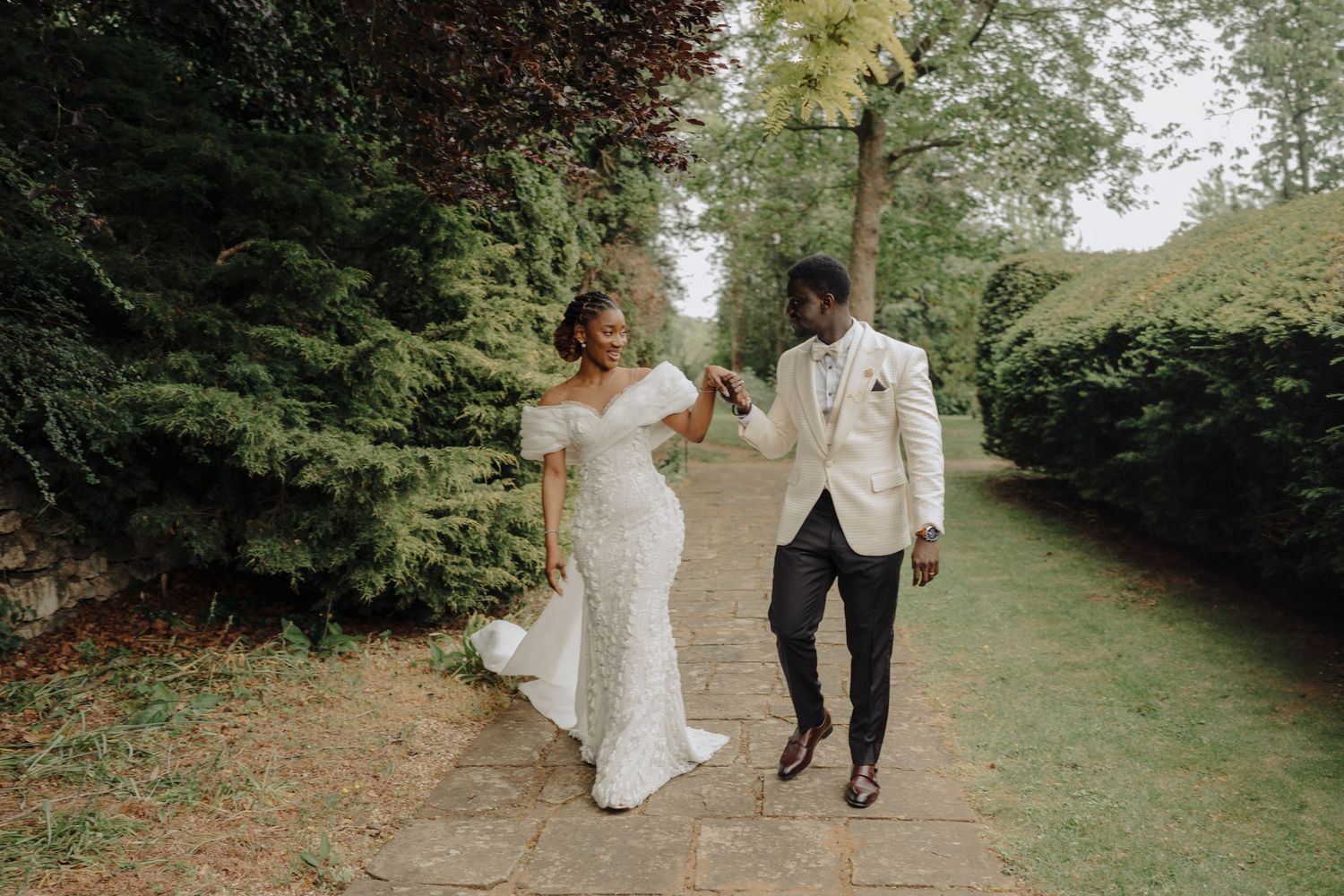 A couple in wedding attire walks together through a lush garden path on their special day.