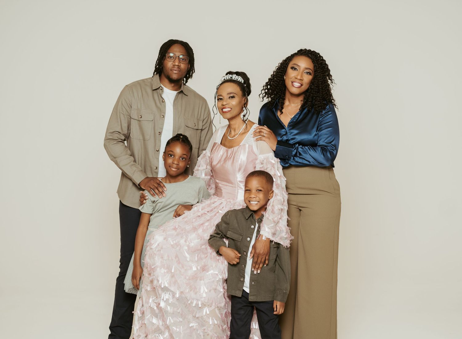 Family photo session with neutral tones and casual poses against studio backdrop.