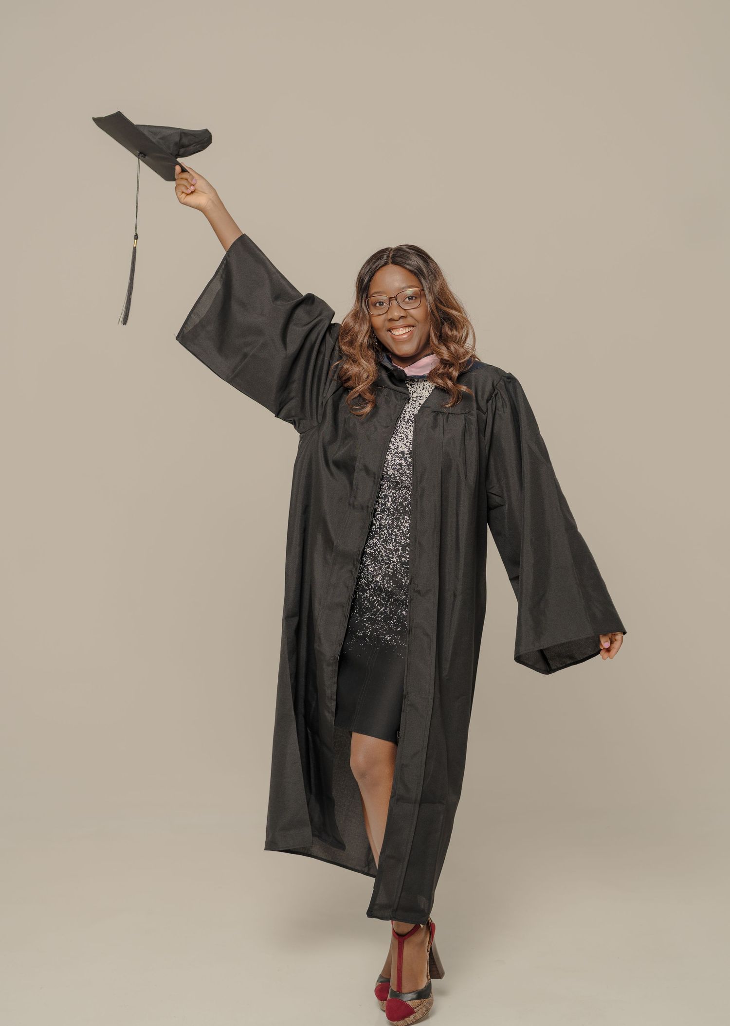 Graduate in black cap and gown poses joyfully during celebration photoshoot.