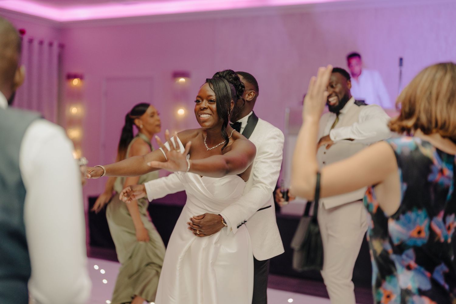 Wedding guests dancing and celebrating on dance floor with purple ambient lighting.