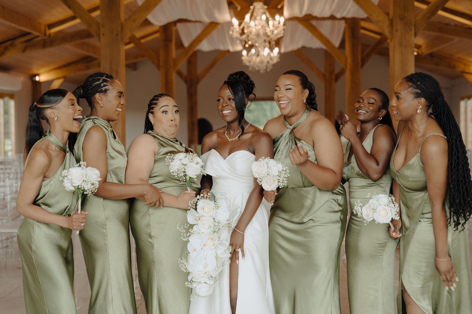 Bridesmaids in sage green dresses stand together in a row at an elegant indoor wedding venue.