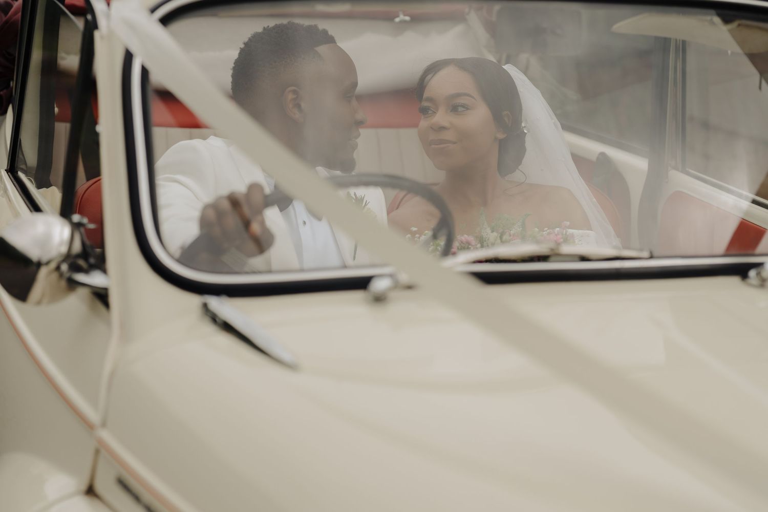 Newlyweds sharing intimate moment inside classic white vintage car.