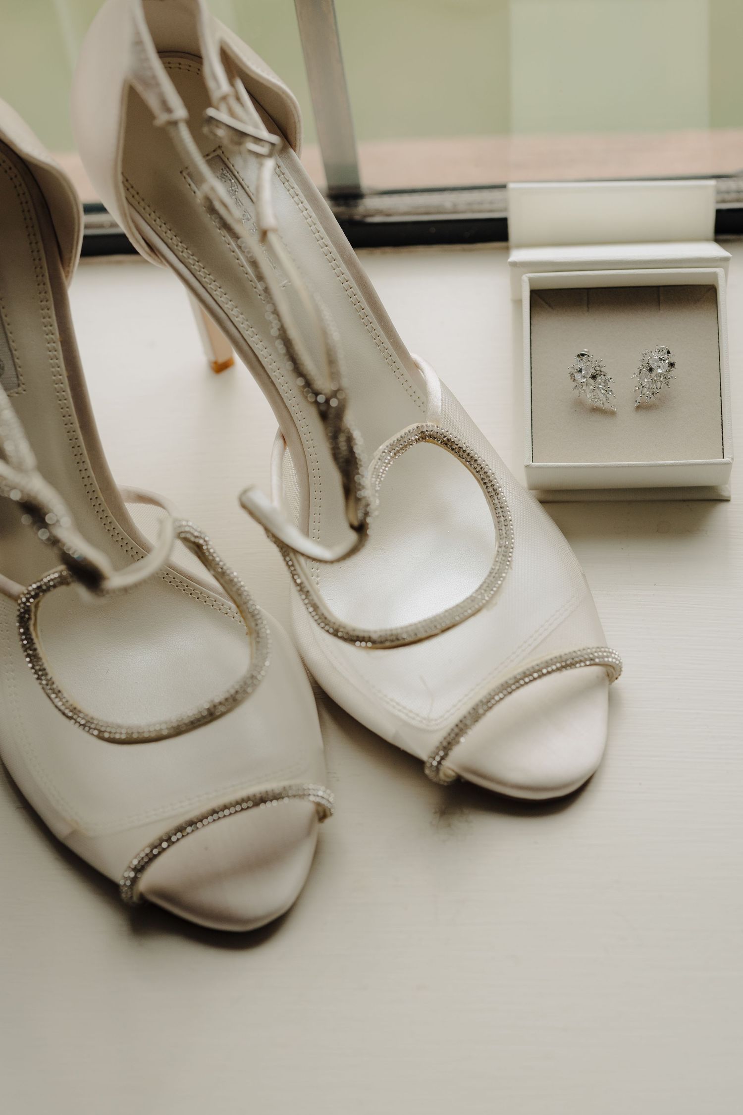 Elegant white bridal shoes with delicate beading and embellishments displayed on a light surface.