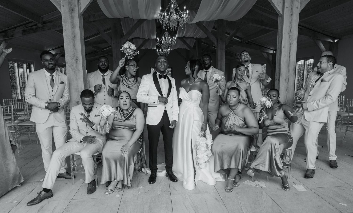 Black and white photo of wedding party members dancing and celebrating in rustic venue.