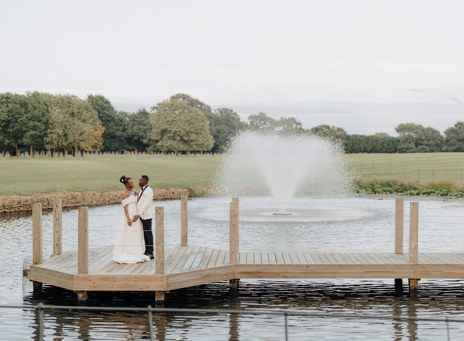 A white wedding ceremony setup on a lakeside dock with water and trees in the background.