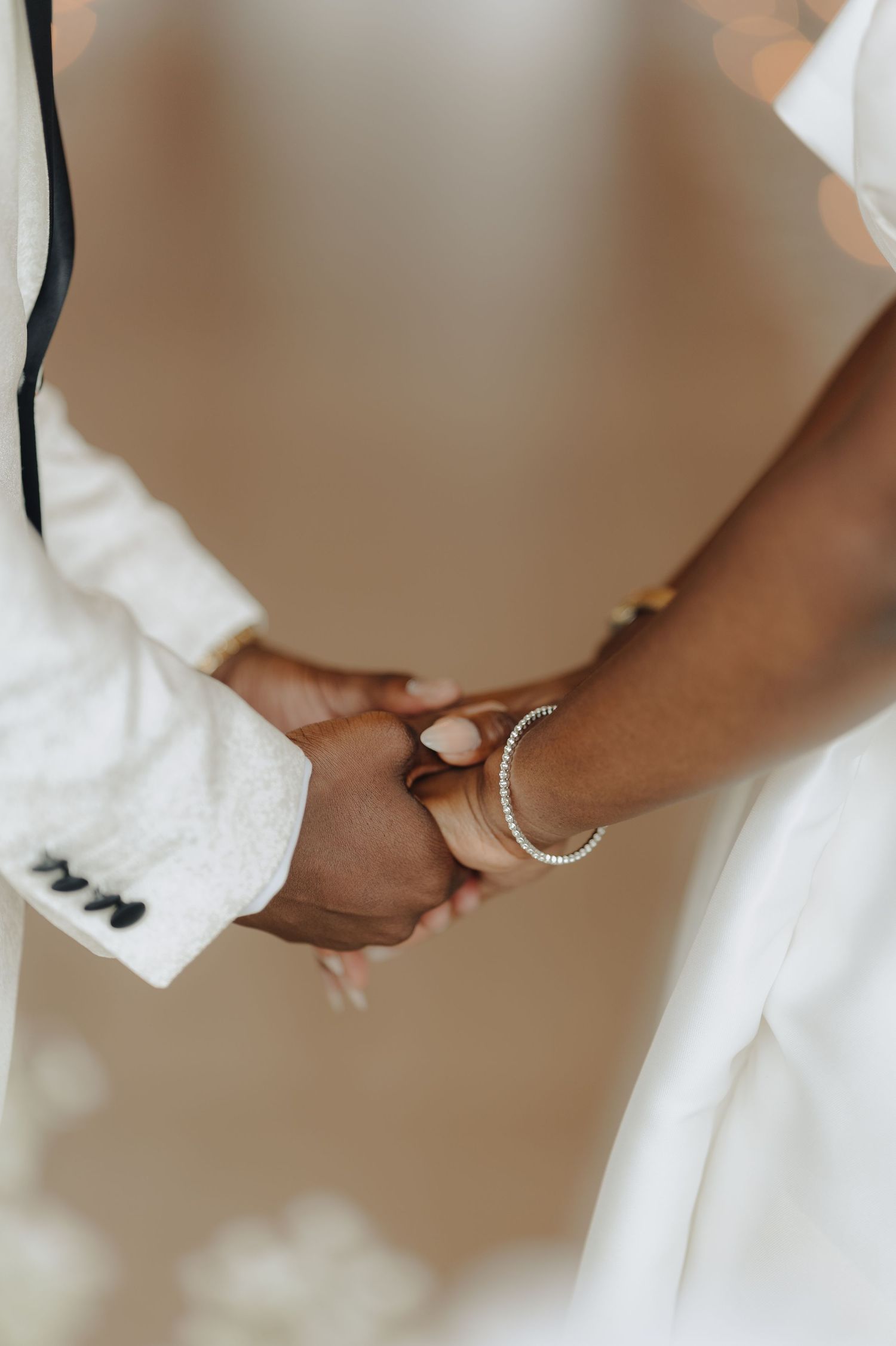 Close-up detail of hands wearing wedding rings and formal white attire.