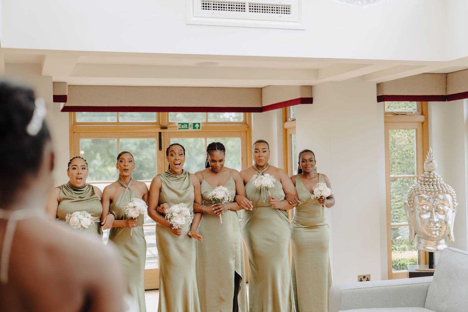 Bridesmaids in matching champagne dresses lined up in a bright indoor venue.