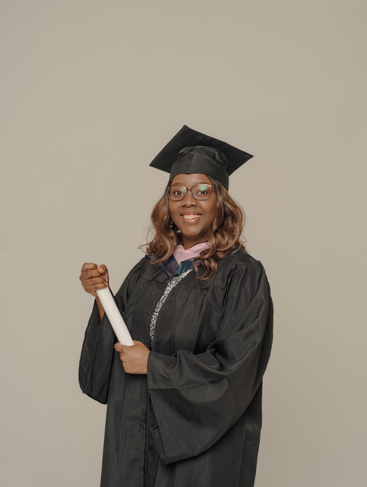 Happy graduate in traditional black academic regalia and glasses celebrates achievement.