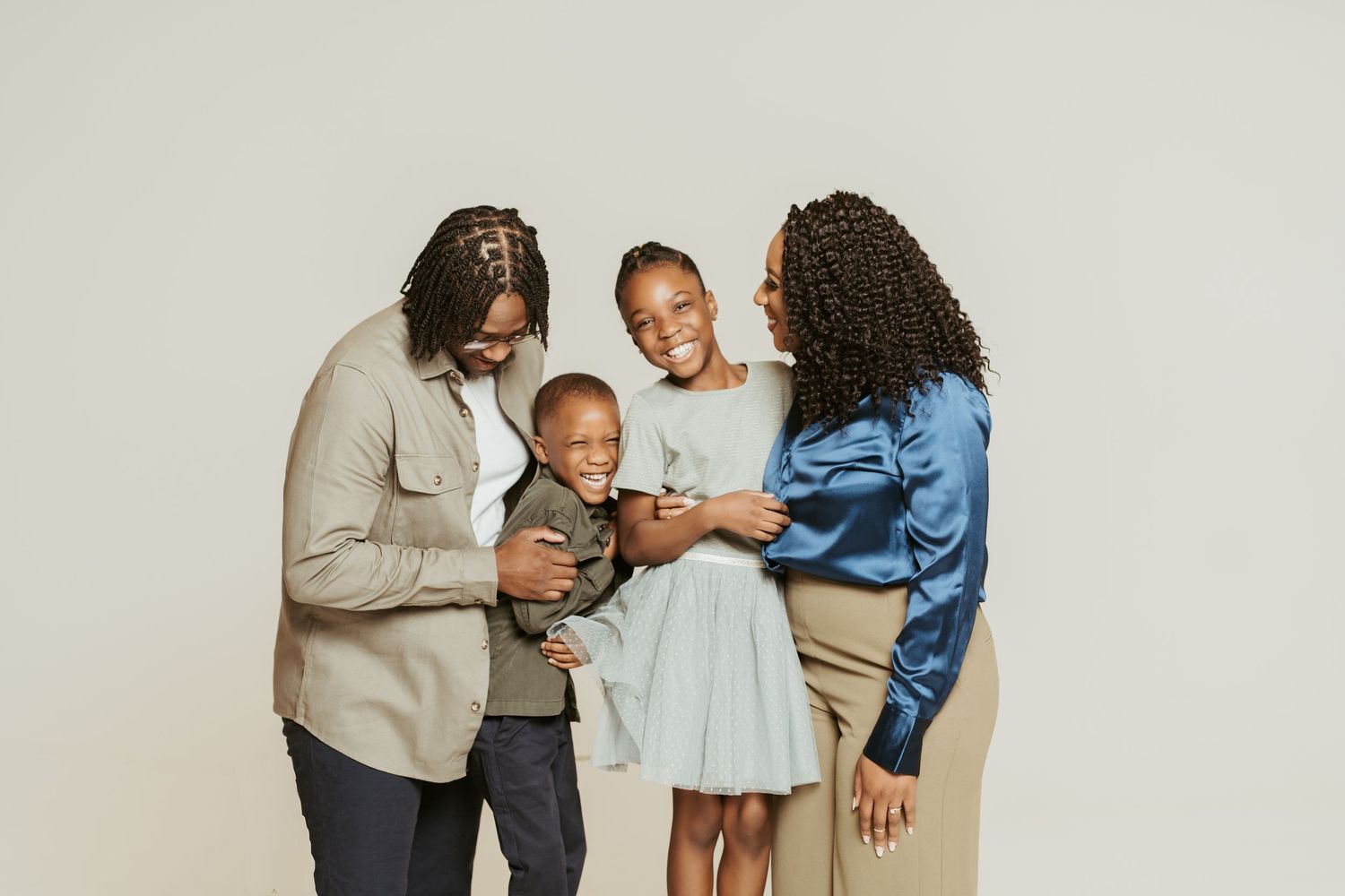 A family of four shares a tender moment together against a neutral backdrop.