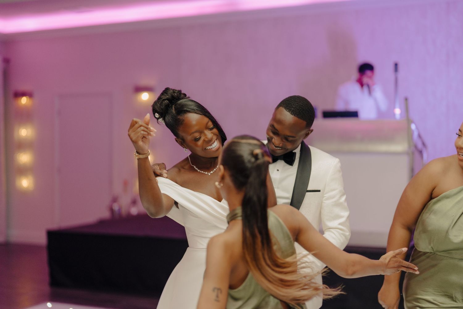 Wedding celebration on dance floor with purple mood lighting and white decor.