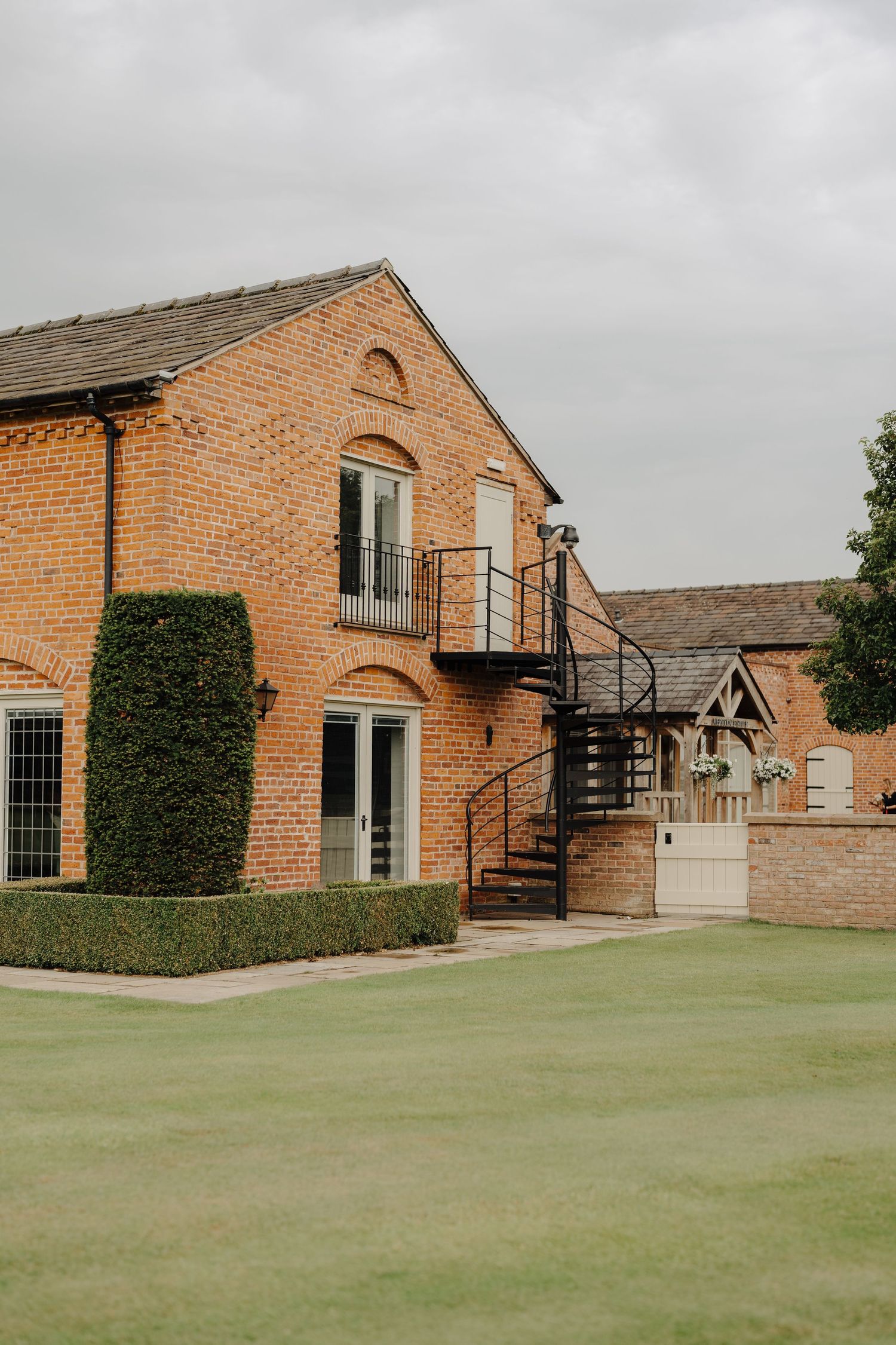 Red brick wedding venue building with green lawn and overcast sky.