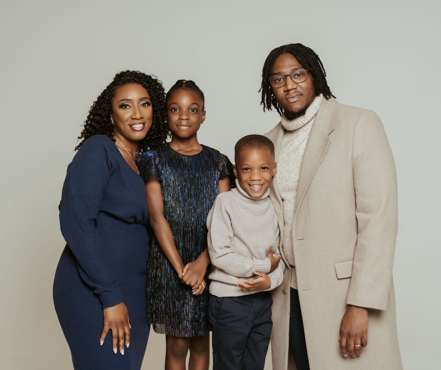 A family of four poses together for a formal portrait against a gray background.