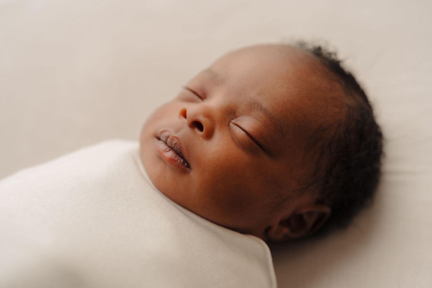Profile views of a sleeping newborn against a neutral beige background.