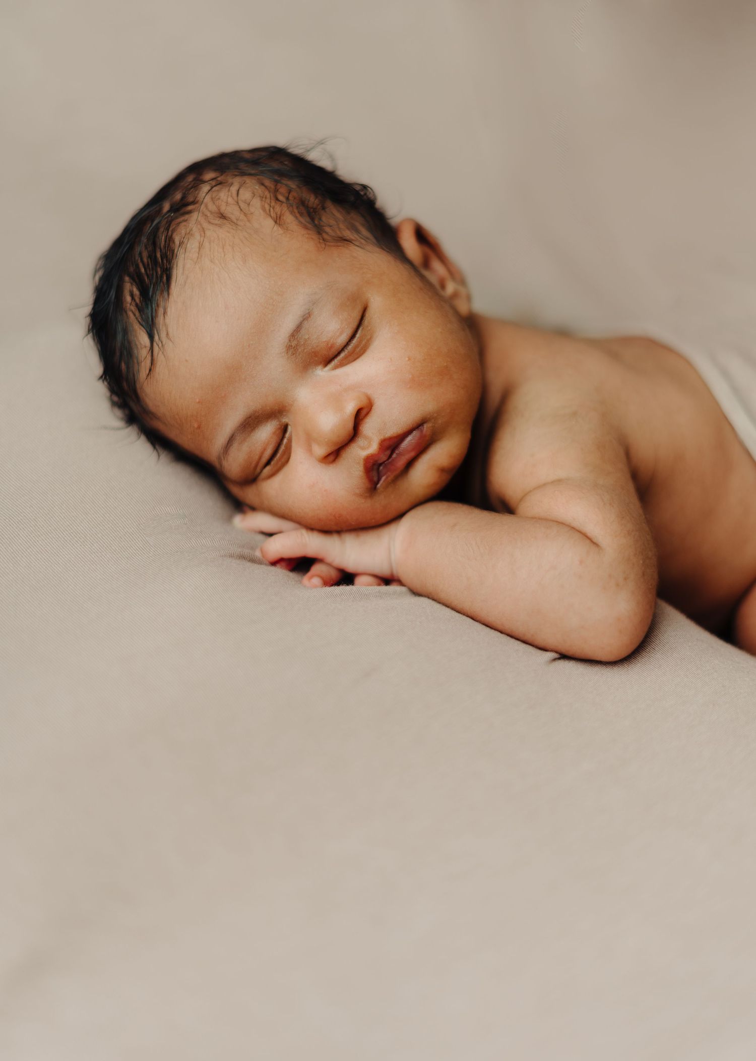 A peaceful sleeping newborn photographed in natural light on beige fabric.