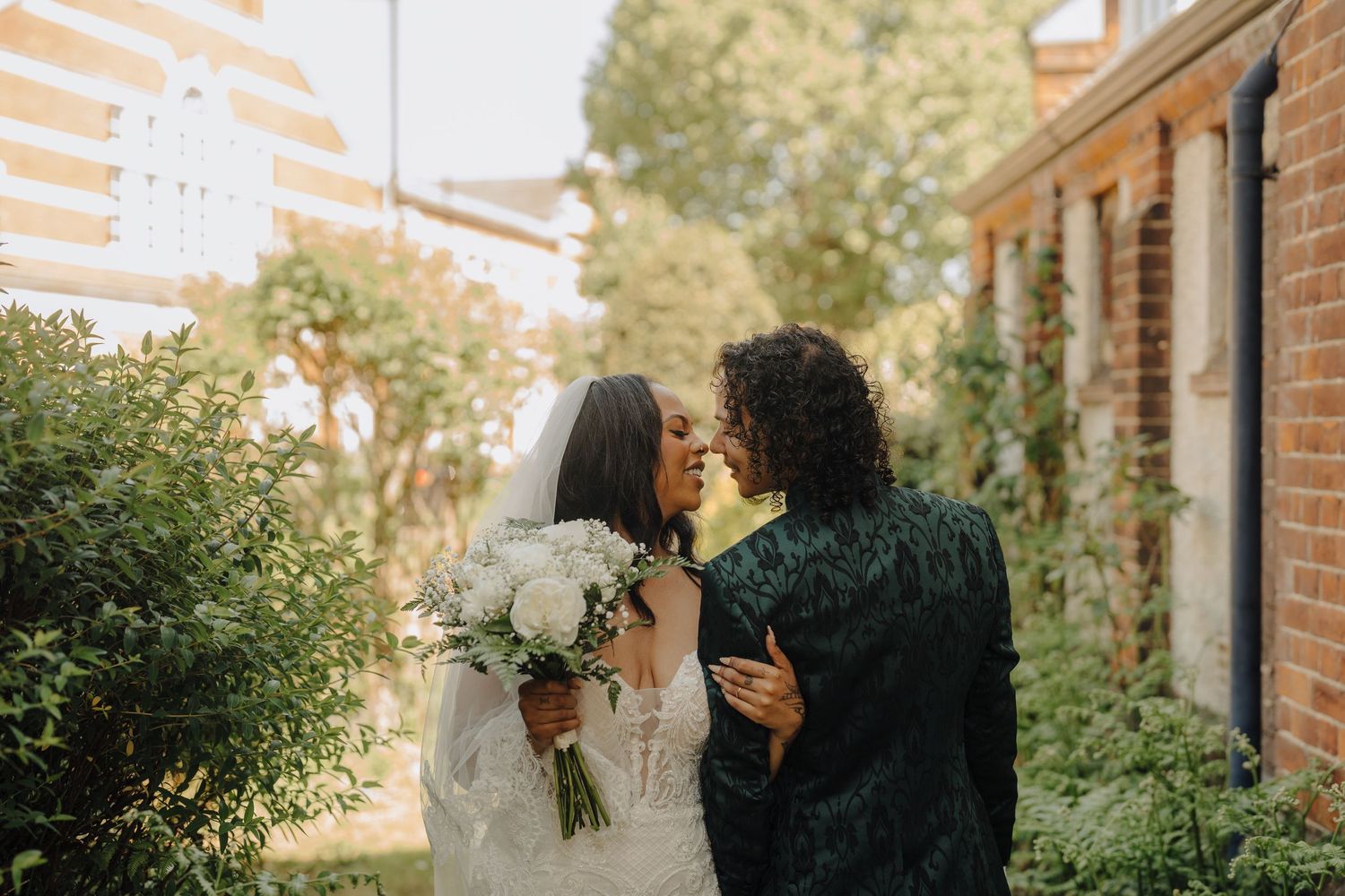 A wedding couple shares intimate moments along a brick building exterior.