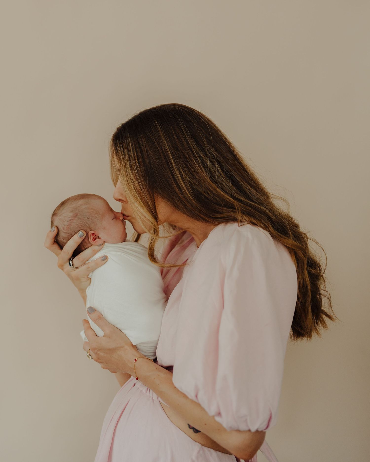 Intimate photo series of mother in pink dress holding and bonding with newborn.
