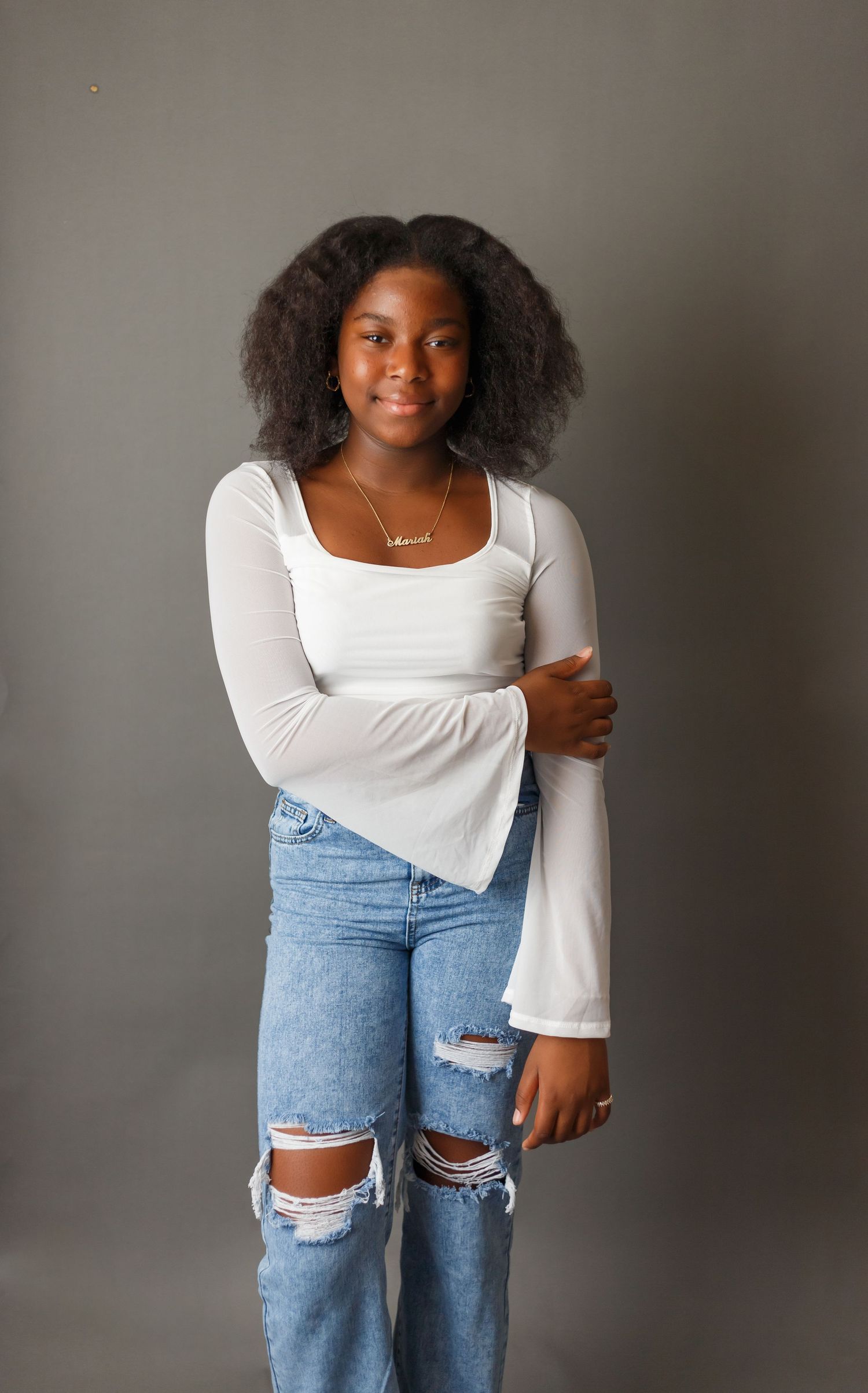 Fashion model wearing white top and distressed denim jeans poses against neutral background.