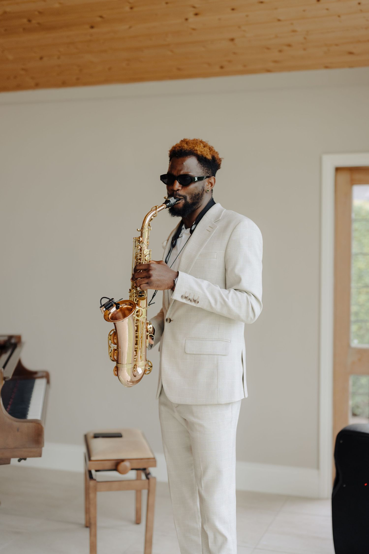 Saxophone performer in a white suit and sunglasses playing during an indoor event.