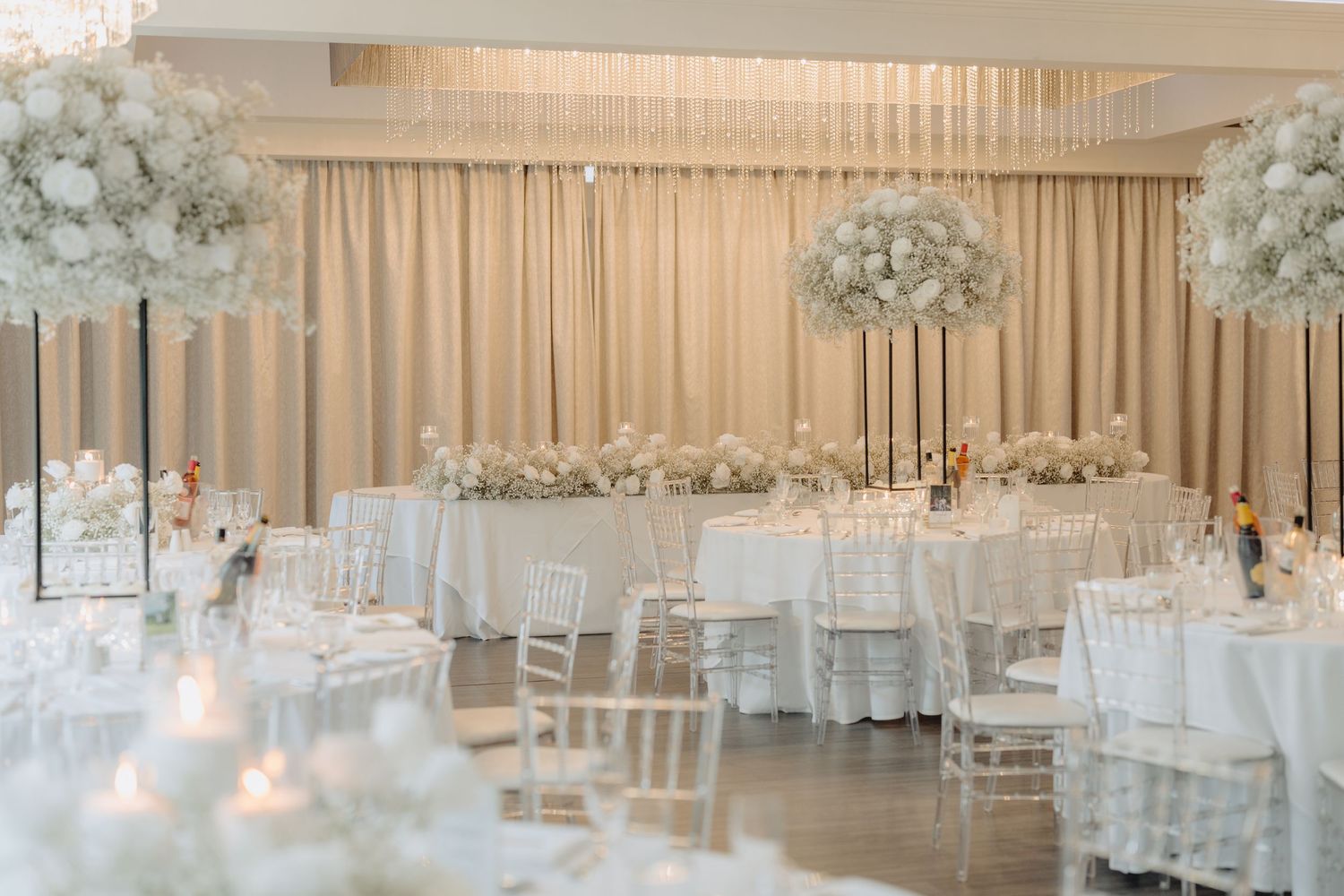An elegant all-white wedding reception room with floral centerpieces and draped fabric decor.