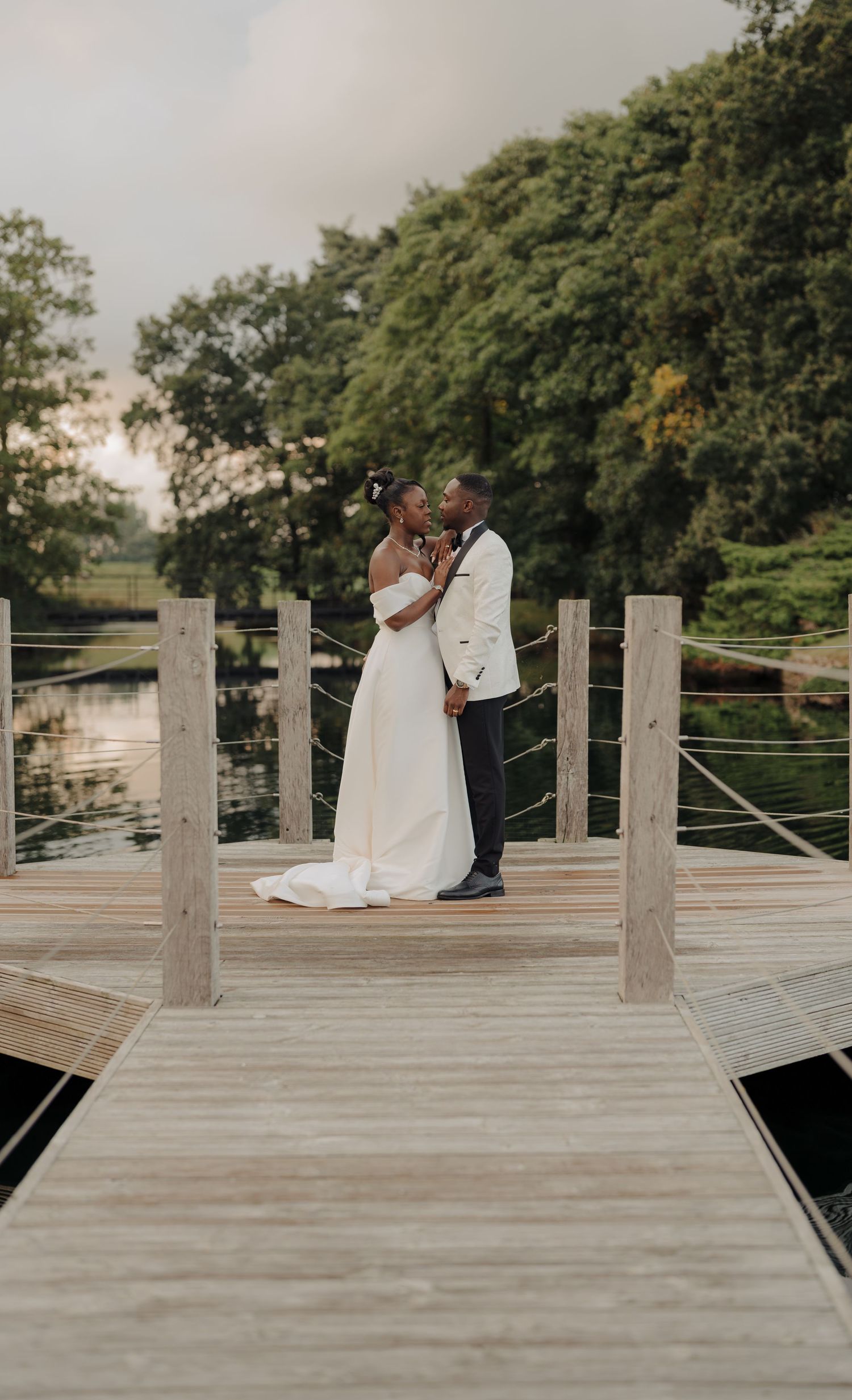 Romantic wedding couple shares intimate moment on wooden dock surrounded by nature.