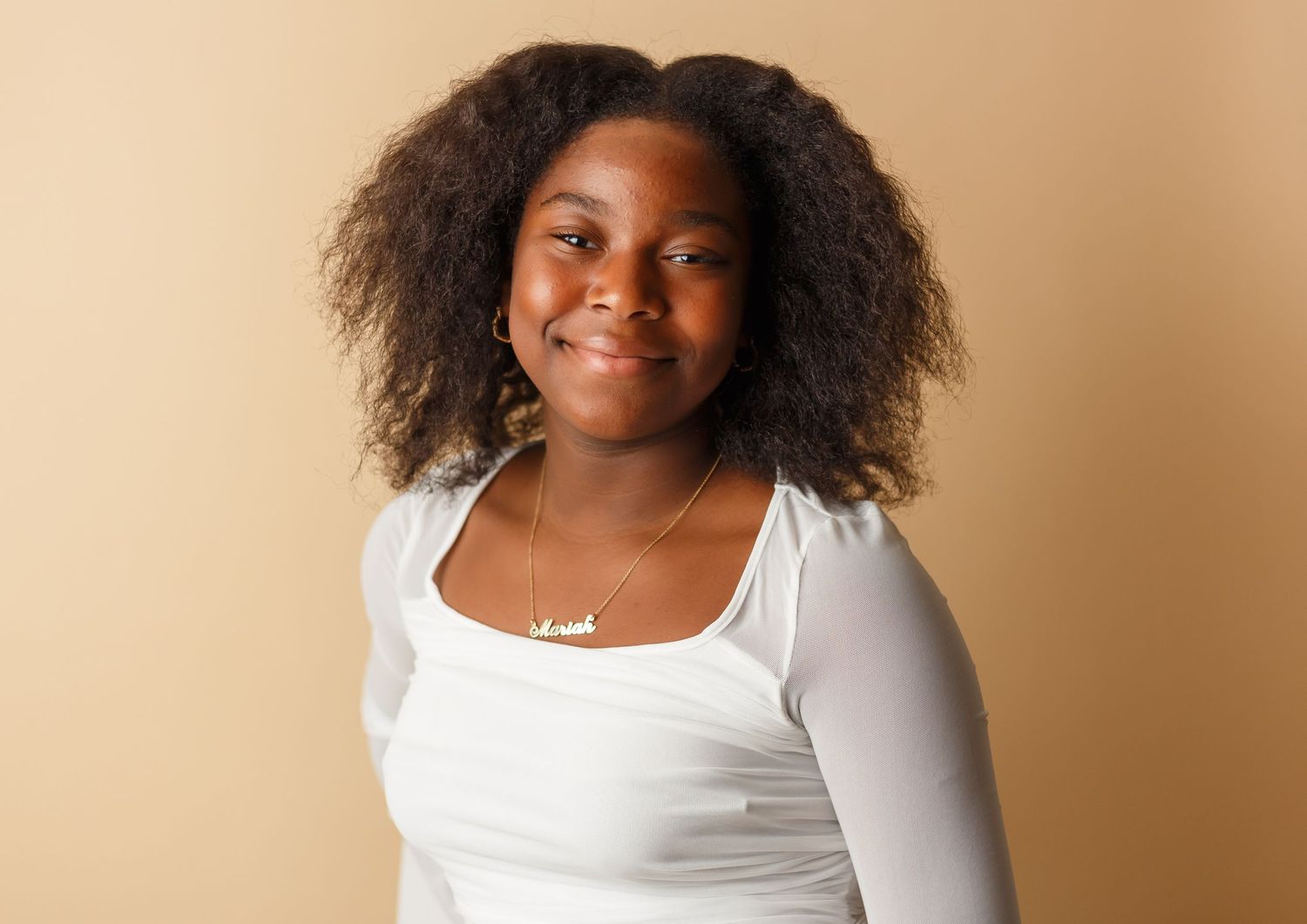 Portrait session against beige background showing casual style with white top and natural hair.