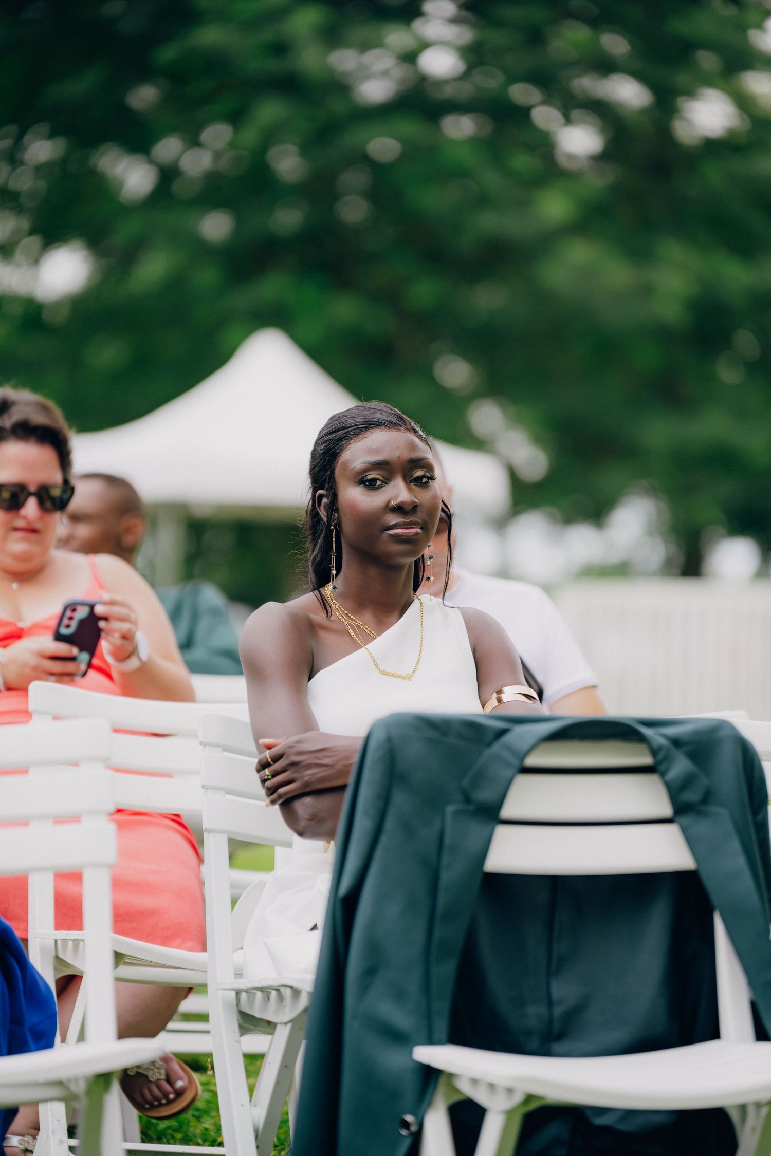 Wedding guests relax in white chairs on a lawn during an outdoor summer celebration.