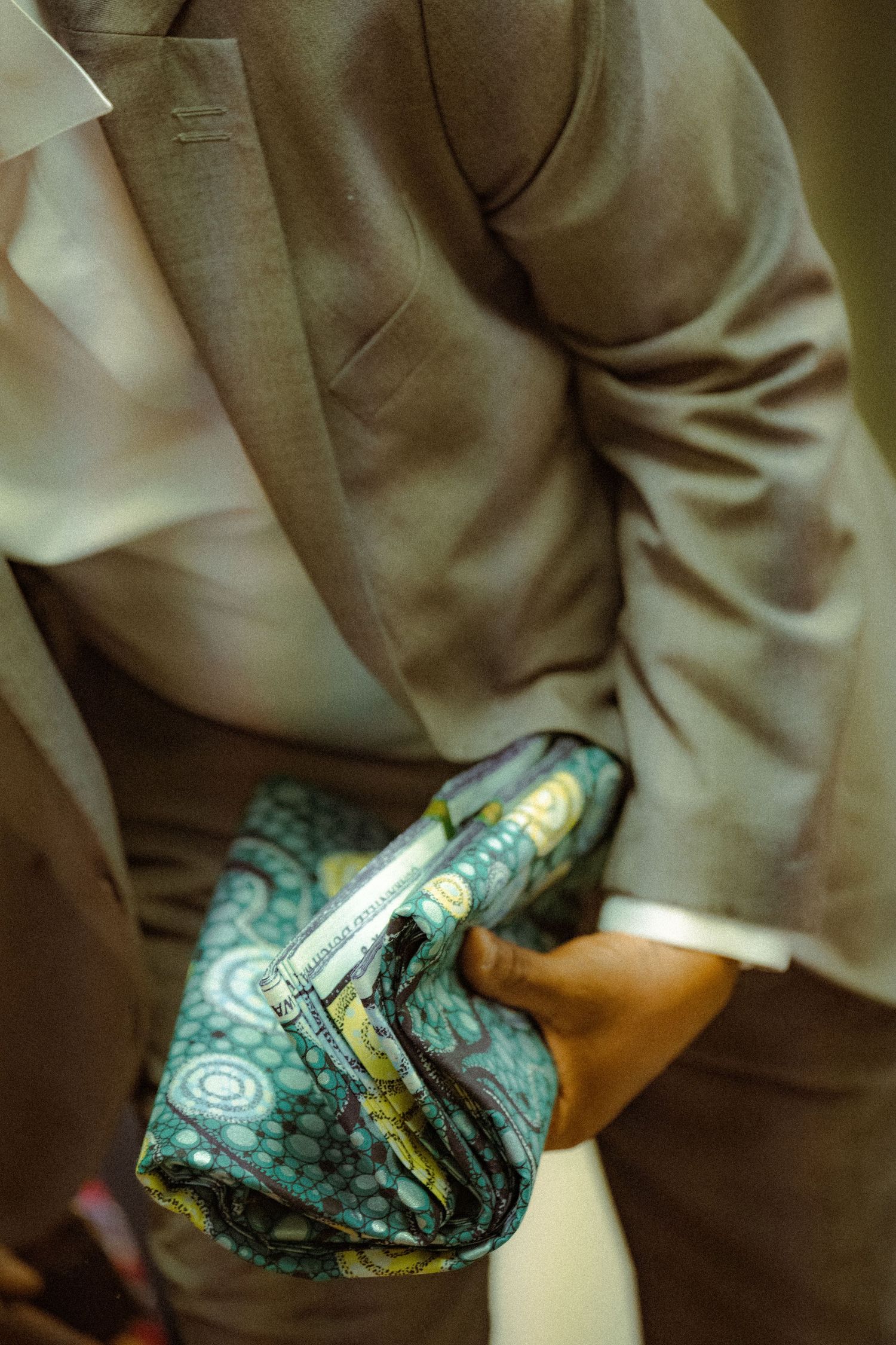 A person wearing a gray suit holds a patterned teal and yellow handkerchief or pocket square.