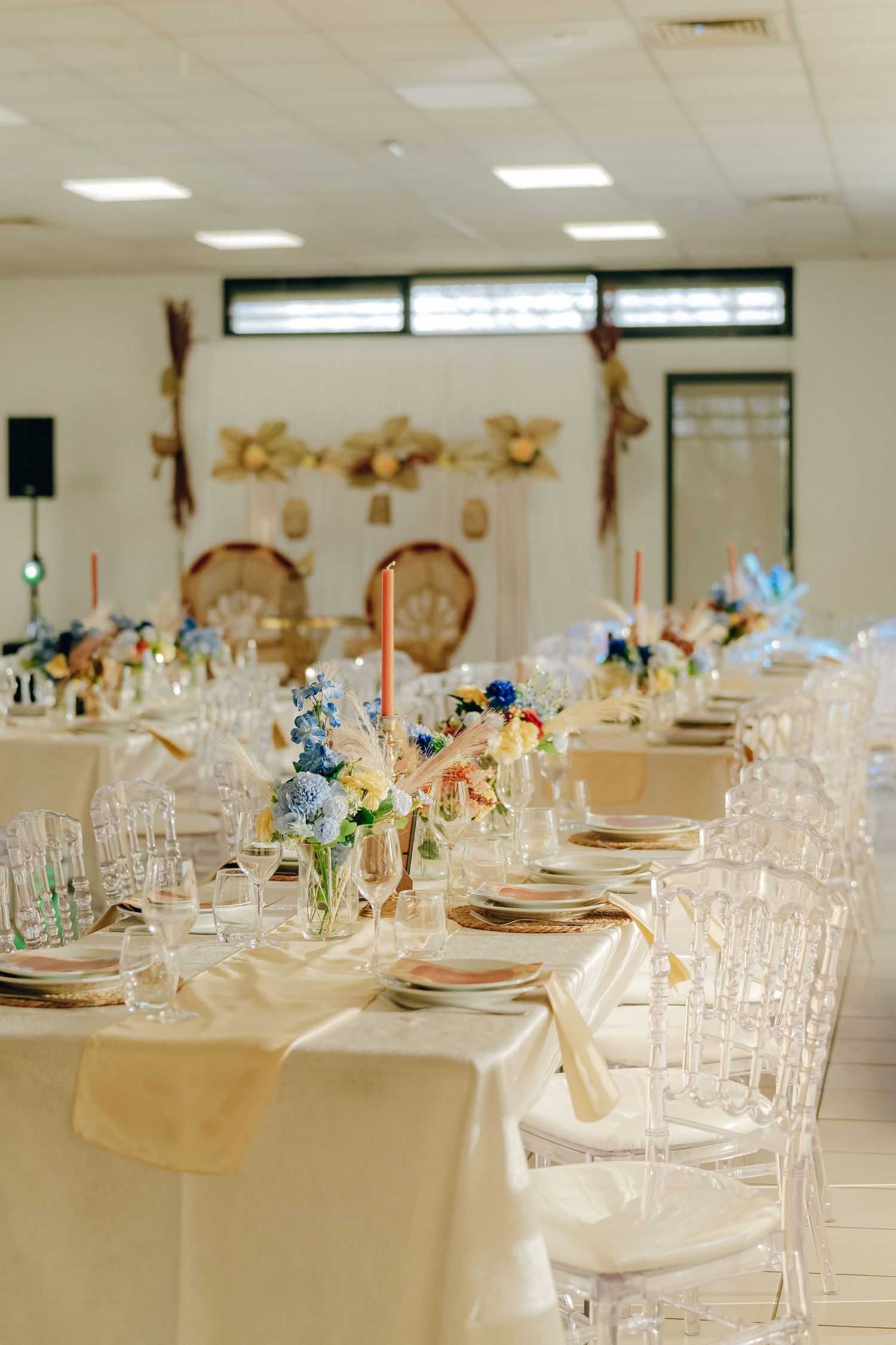 Elegant wedding reception table setup with clear ghost chairs, white linens, blue floral centerpieces and gold accents.