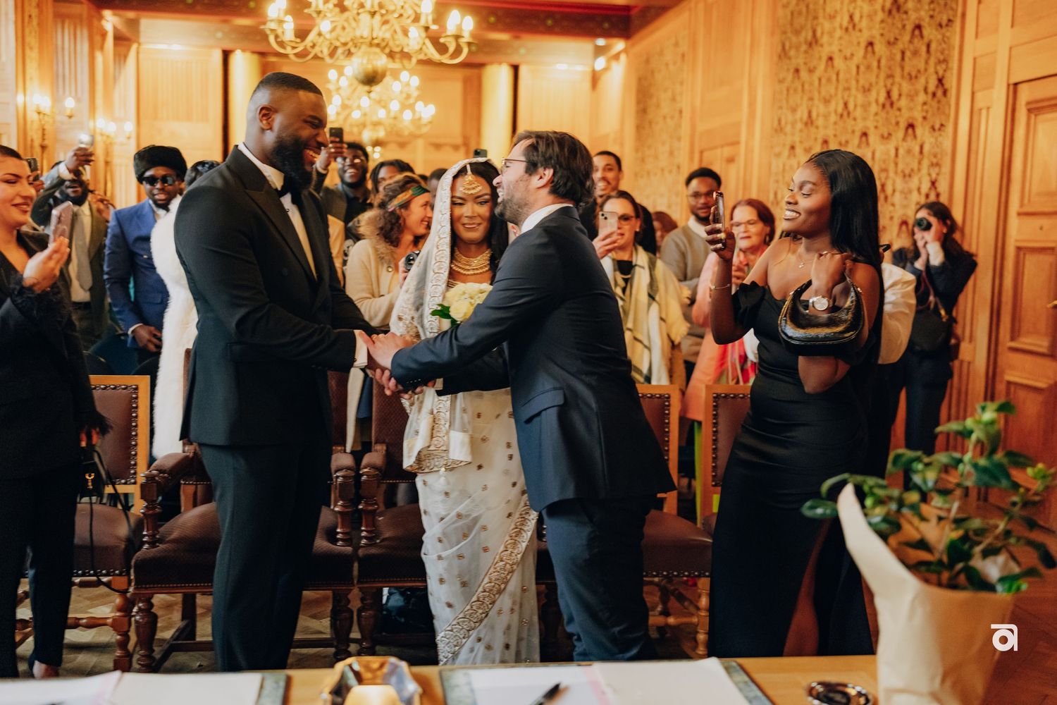 Wedding ceremony in an elegant room with chandelier as couple exchanges vows surrounded by guests.