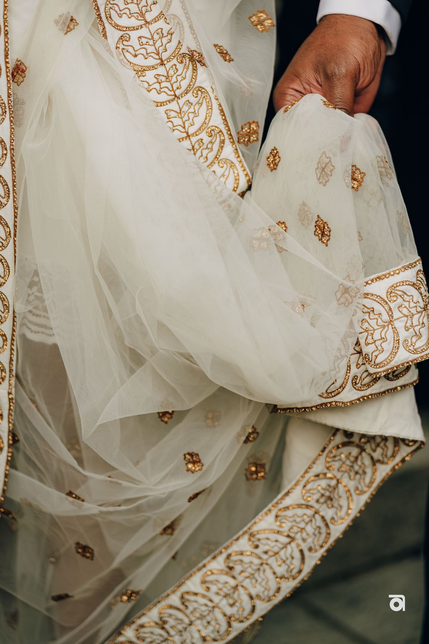 Close-up detail of intricate gold embroidery on white wedding dress fabric.