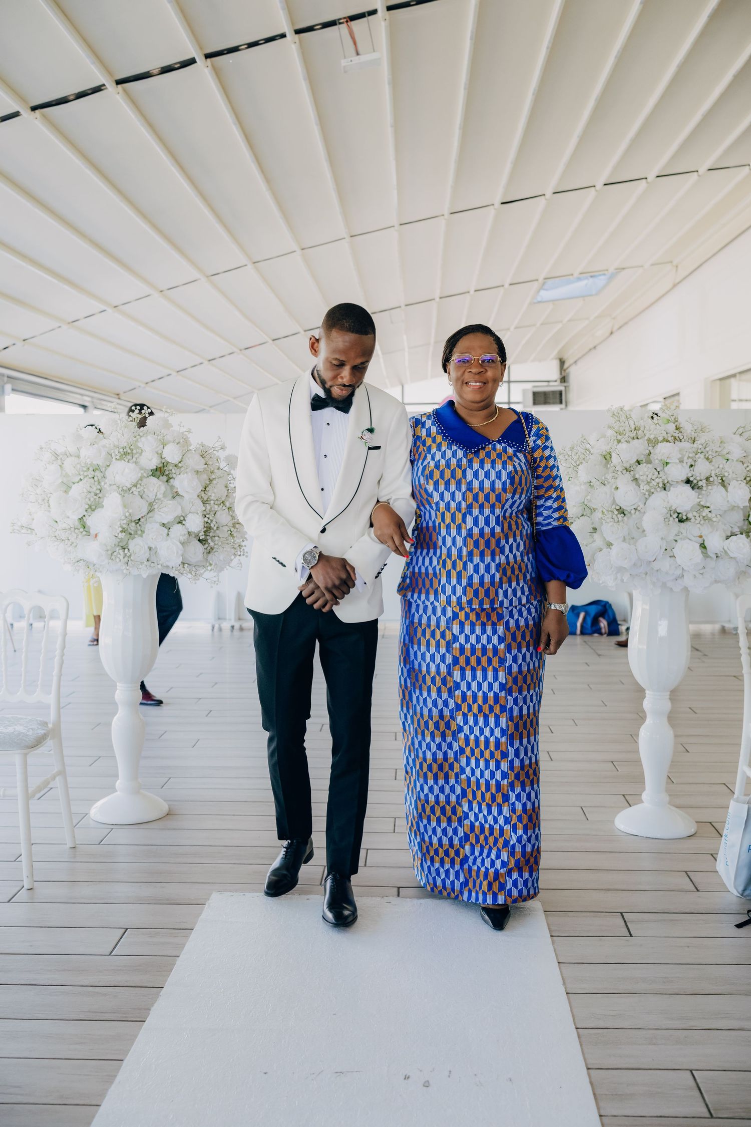 Wedding party members walking through an elegant white venue decorated with floral arrangements.