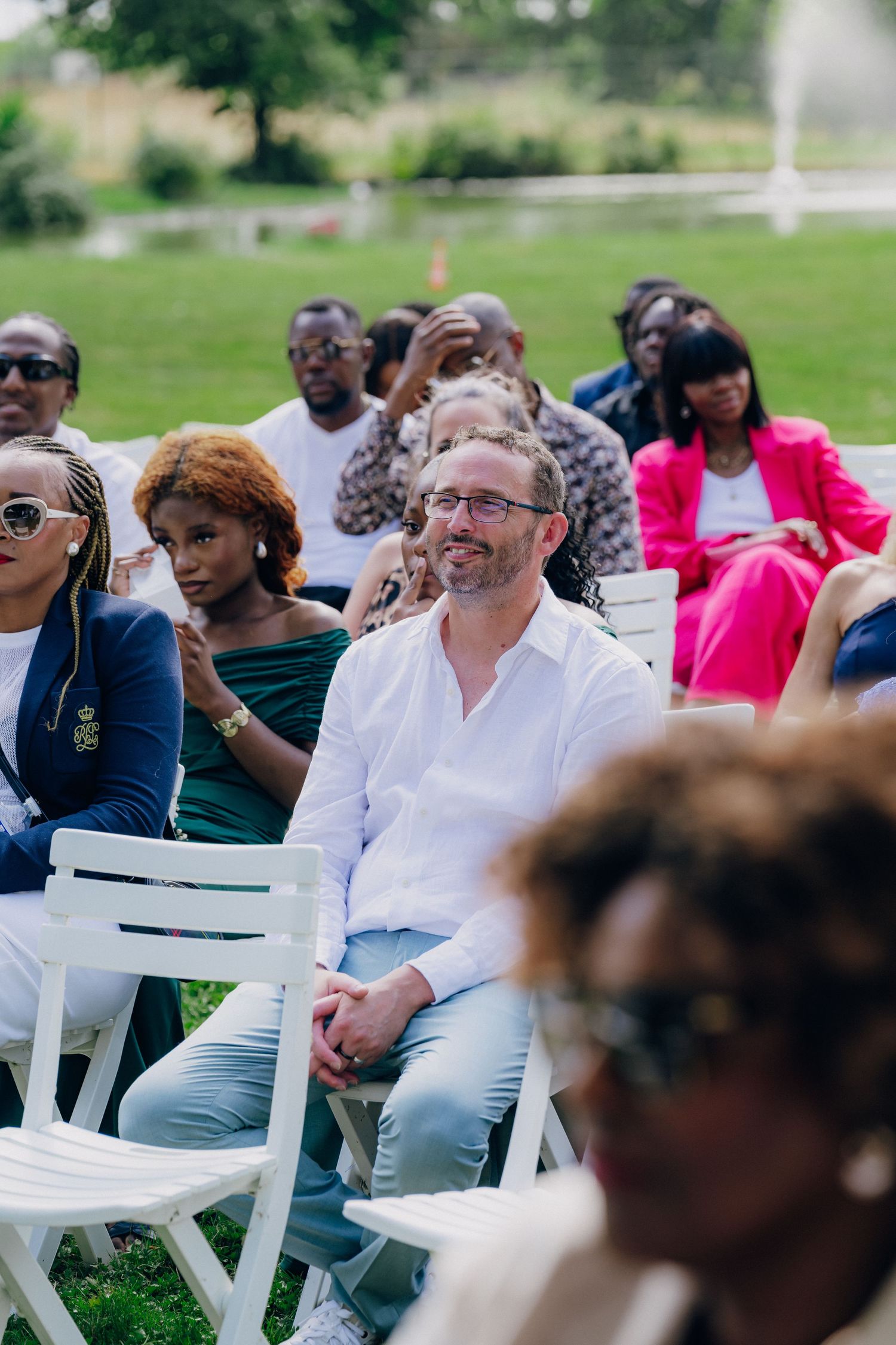 Wedding guests seated in white chairs during an outdoor ceremony with a mix of formal attire.