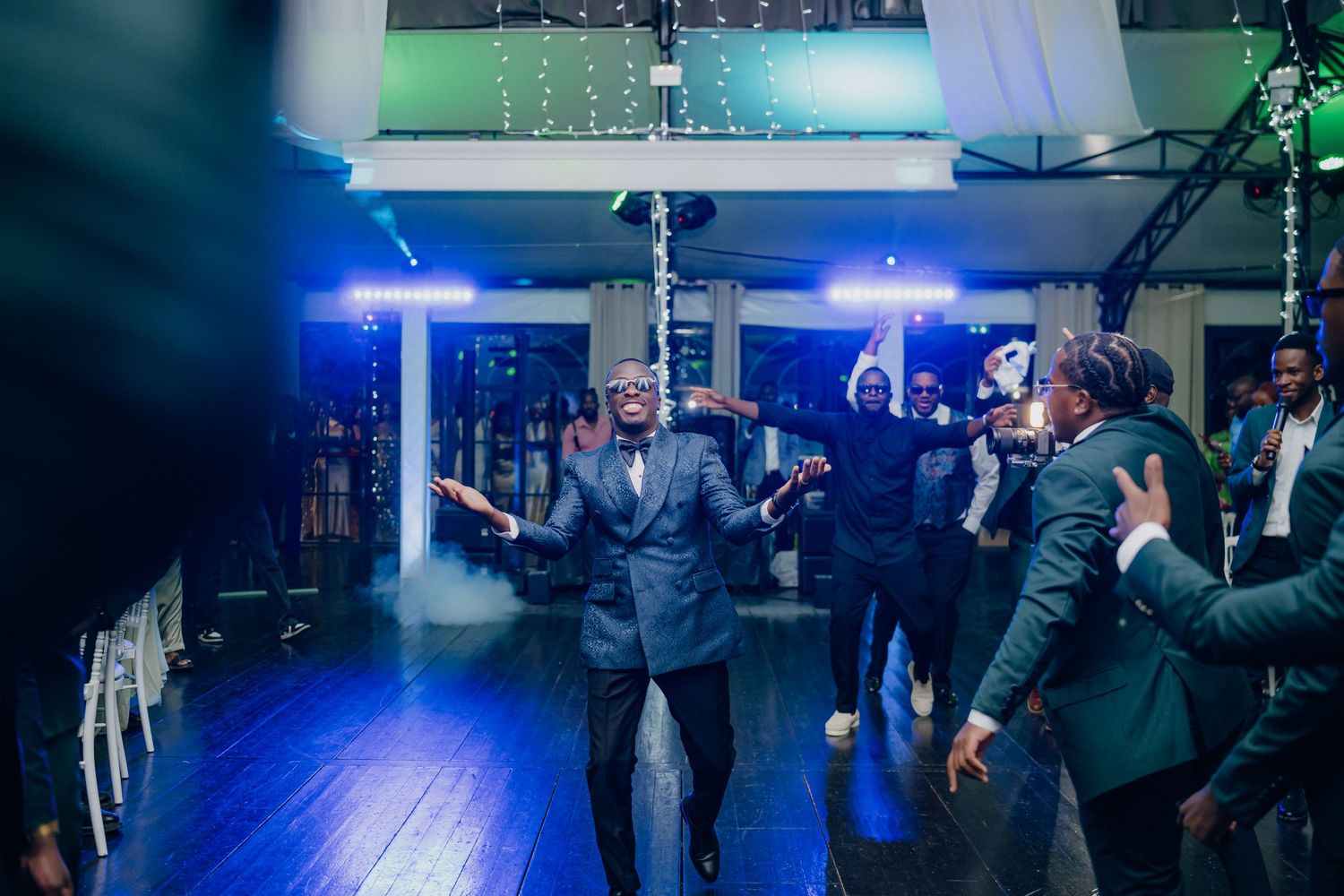 Wedding guests dancing on a dark dance floor illuminated by blue lights during an evening reception celebration.
