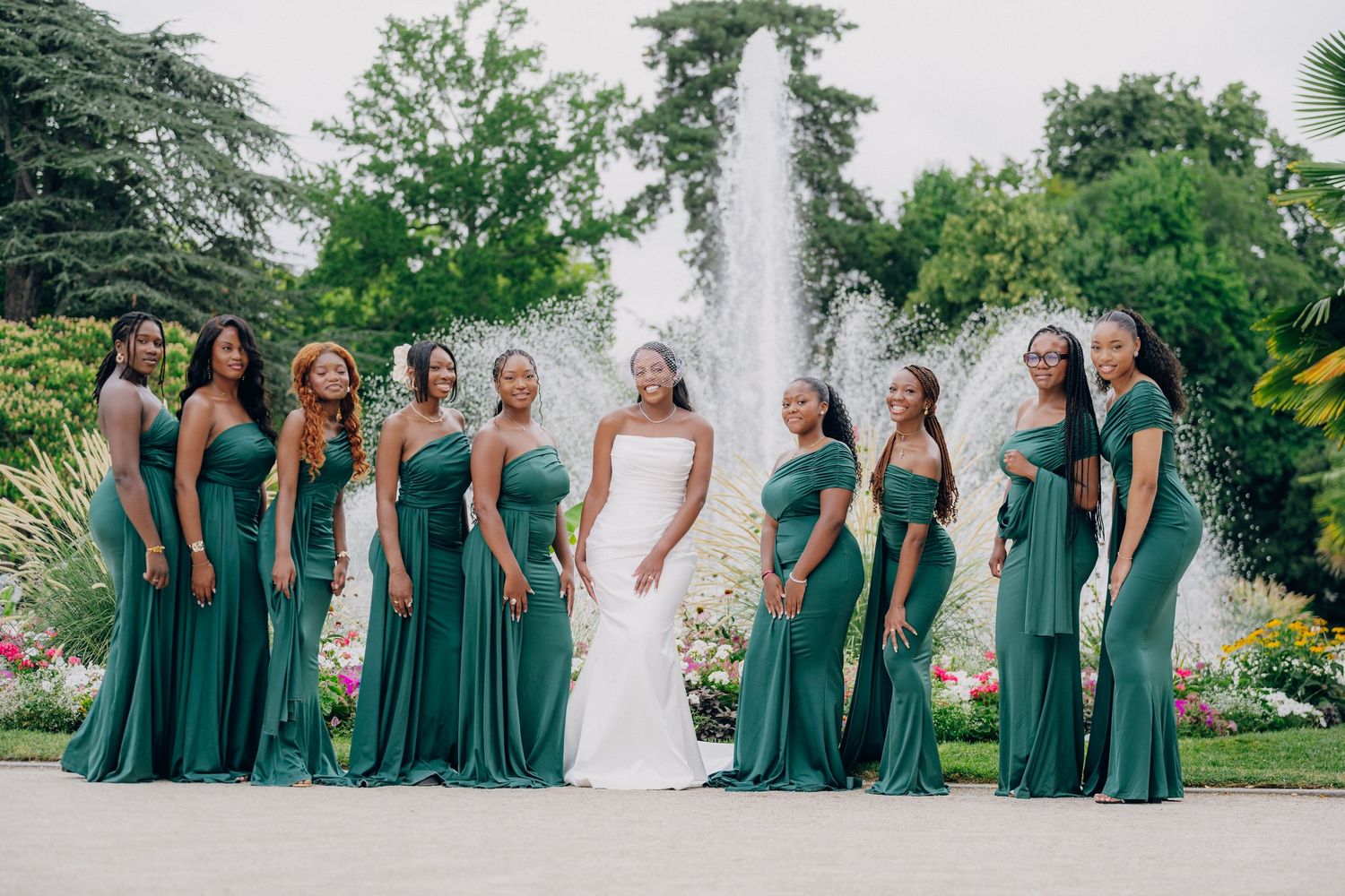 Wedding party poses outdoors in coordinated emerald green bridesmaid dresses and white bridal gown.