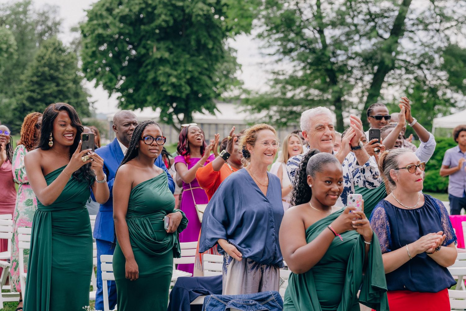 Wedding guests in formal attire watching ceremony from outdoor seating area.