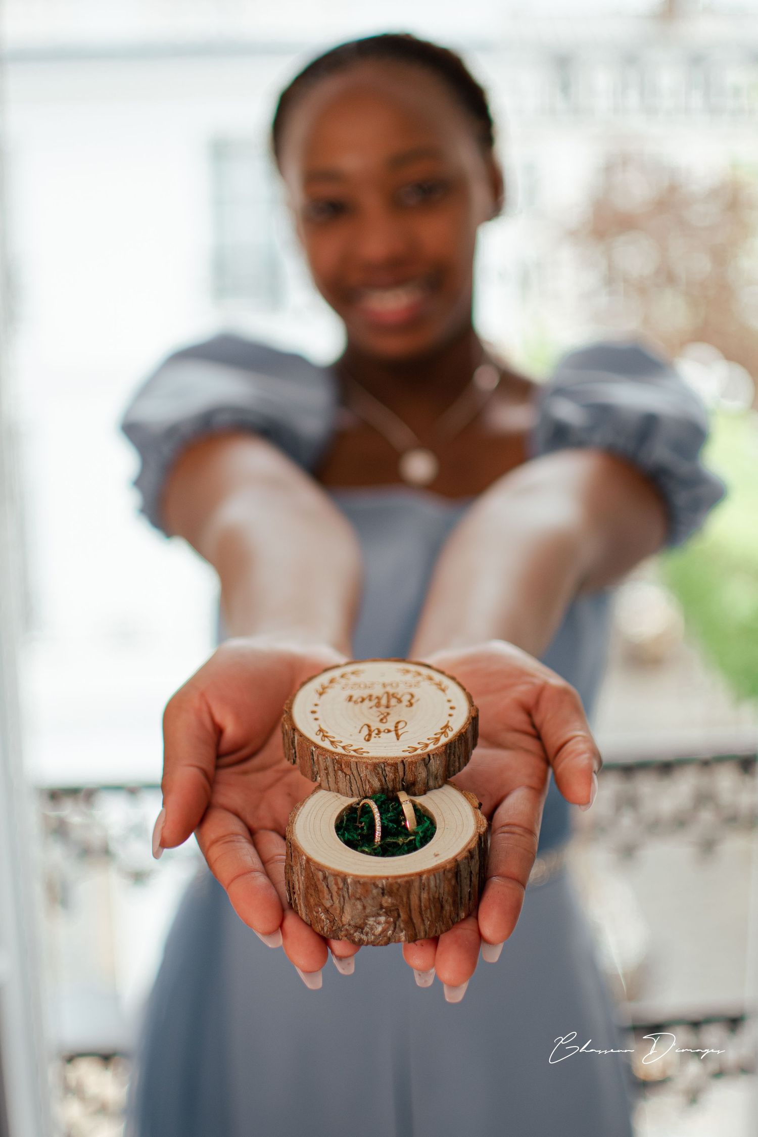 Hands holding a rustic wooden ring box with wedding rings.