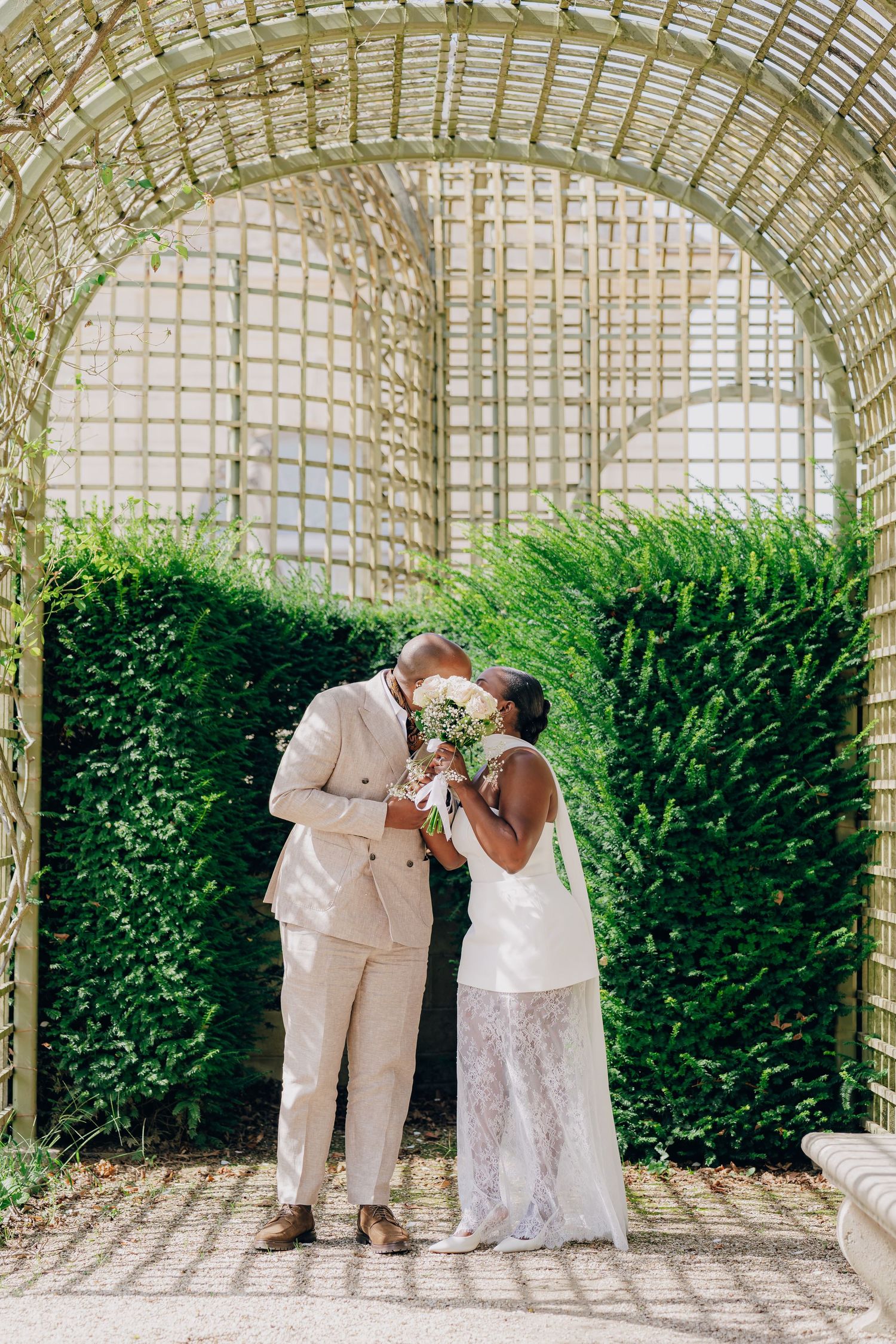 A couple shares a romantic moment under an elegant garden trellis archway surrounded by lush greenery.