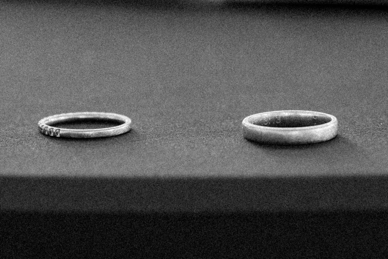 Black and white close-up photograph showing a wedding ring casting a dramatic shadow on a textured surface.