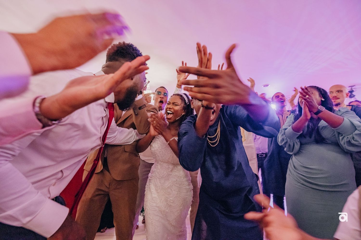 Energetic wedding party dancing and celebrating on the dance floor with purple ambient lighting.