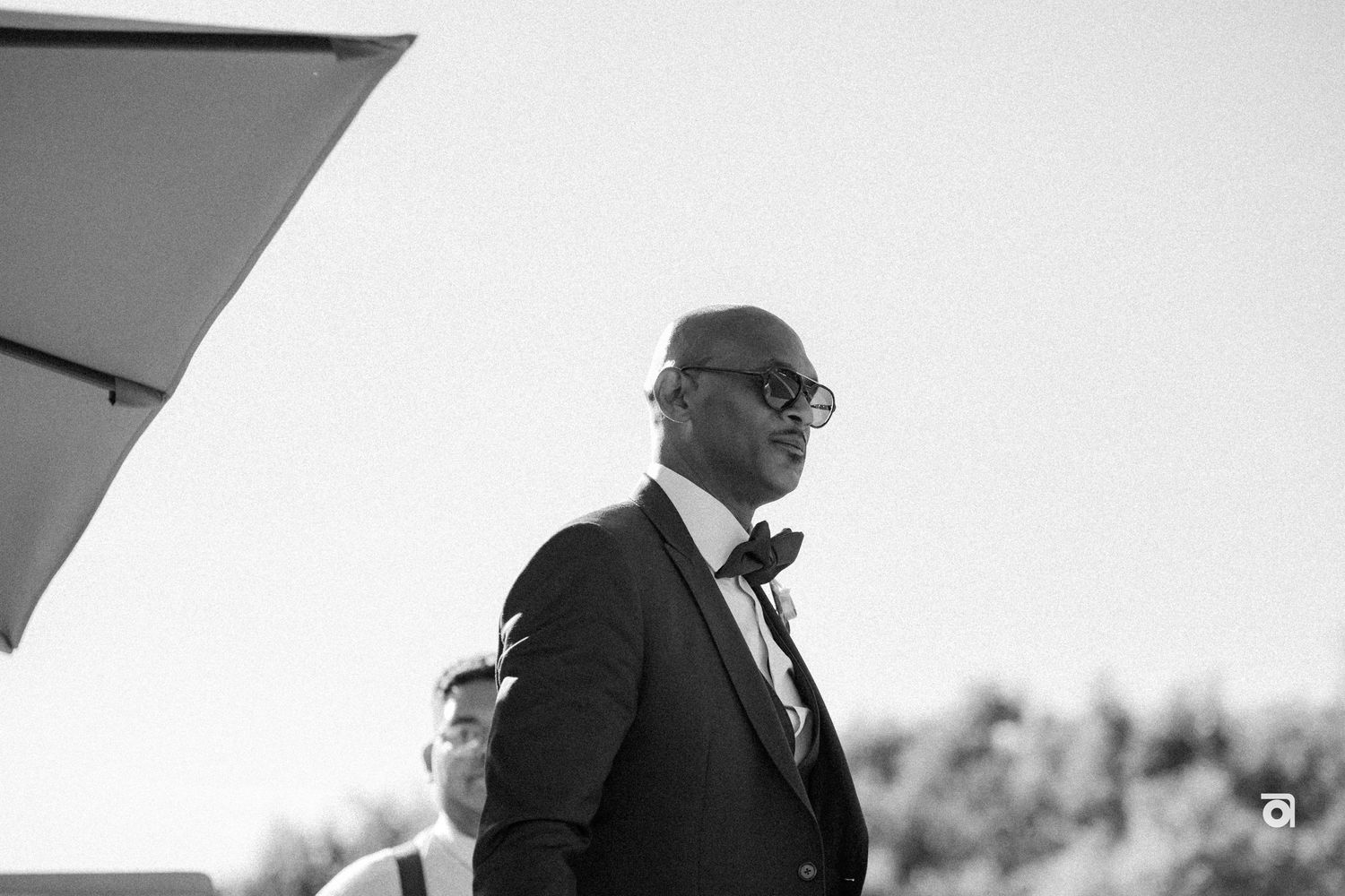A well-dressed figure in a suit and glasses looks off into the distance in this black and white photo.