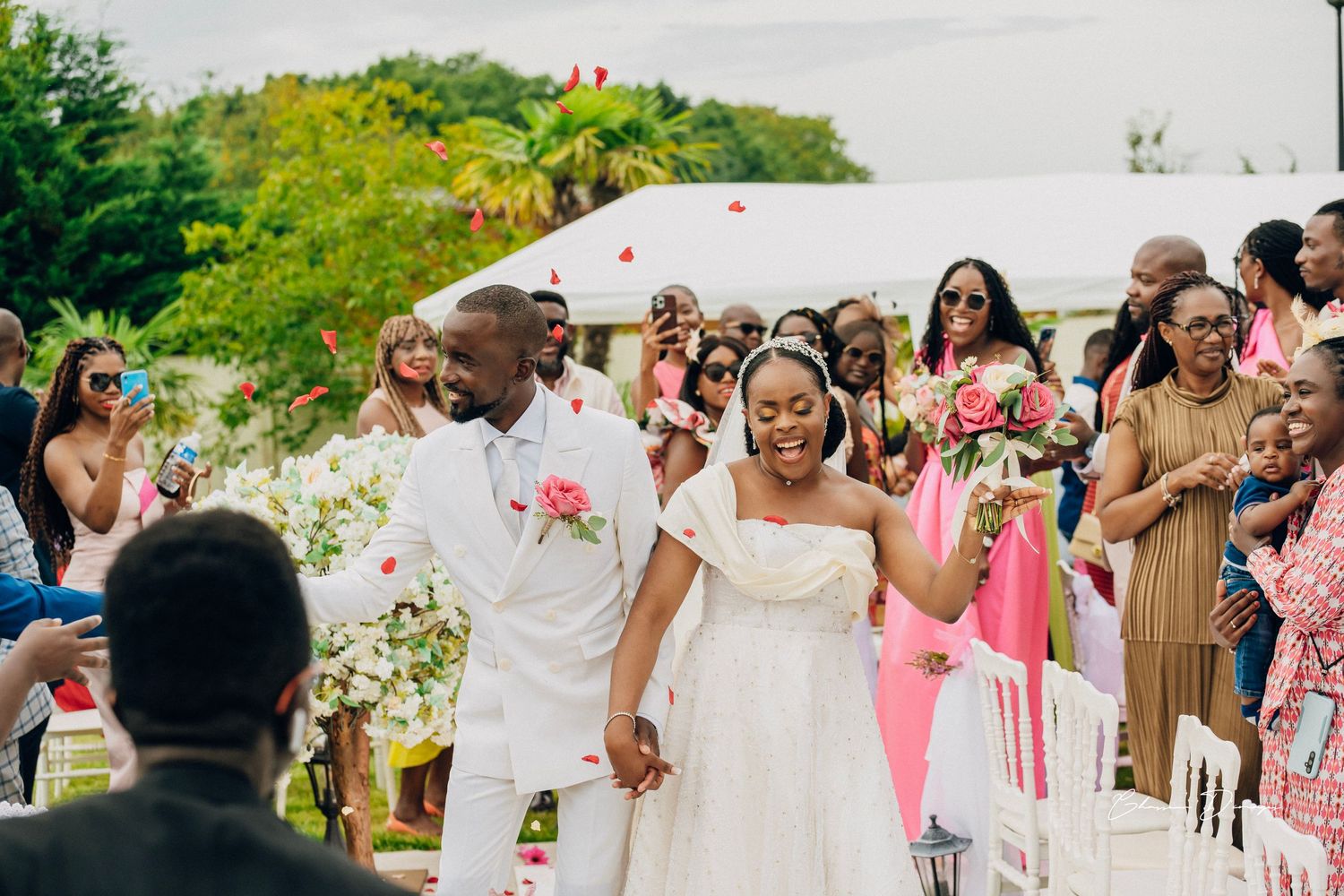 Happy couple walking down the aisle at outdoor wedding with pink-clad guests.