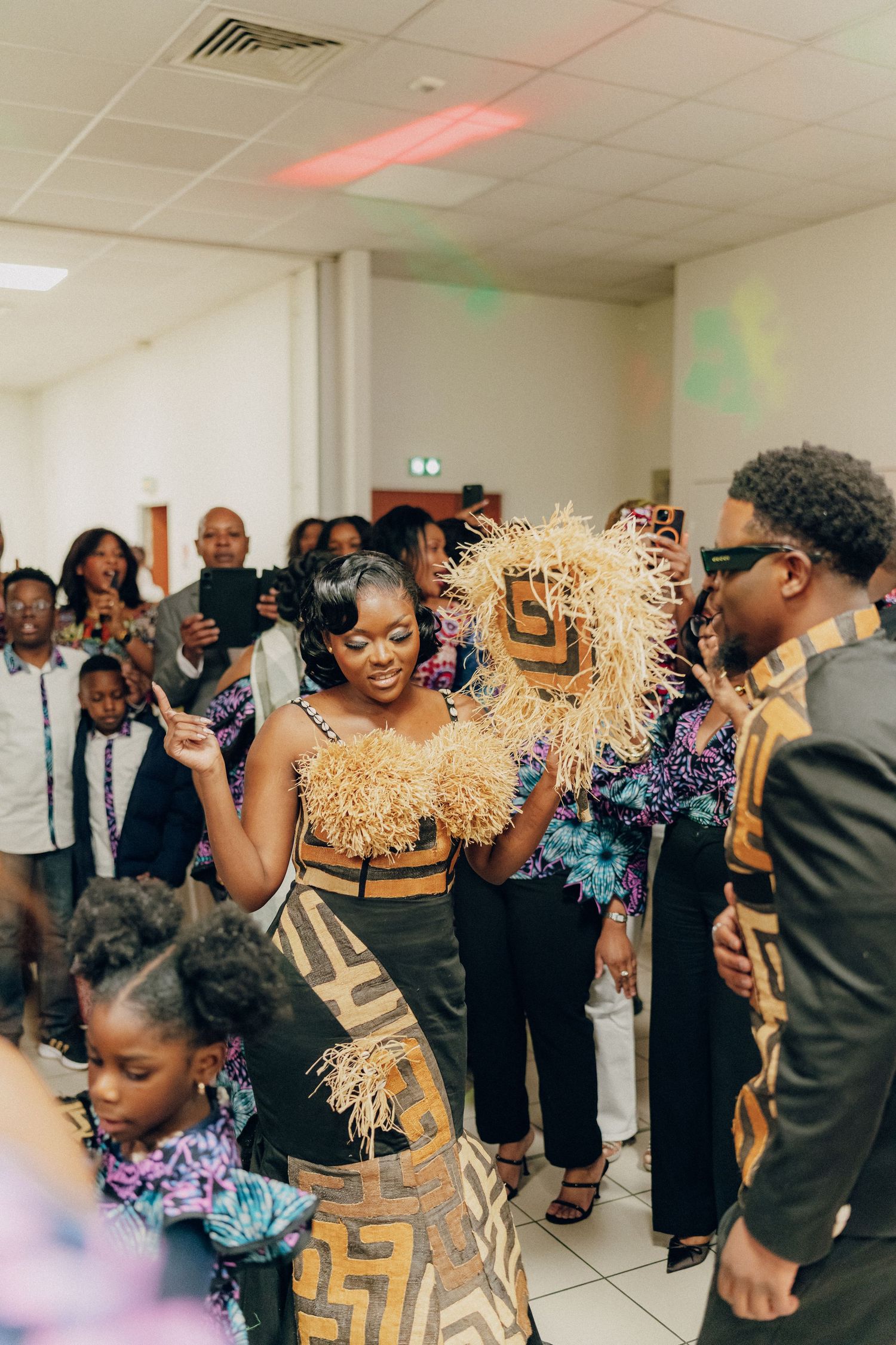 A celebration in a hall with people wearing coordinated gold and black patterned traditional African attire.